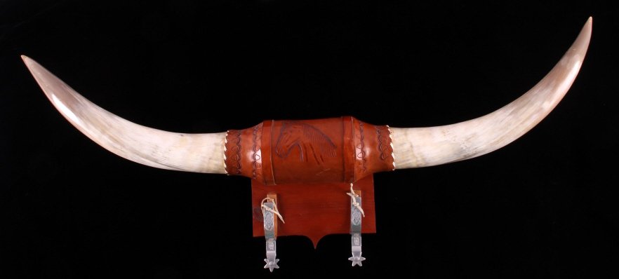 Steer Horn and Spur Hat Rack: This is a steer horn and spur hat rack. The rack is made with a pair of steer horns that features a leather center piece. The leather shows a hand tooled horse design. The spurs are aluminum etched wi