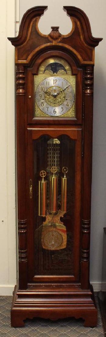 Howard Miller Tall Case Clock: Cherry case with a broken arch pediment, turned reeded columns on a shaped base, 8 day brass works with moon phase me three chimes, 85"h x 24"w x 14"d. Missing finial.