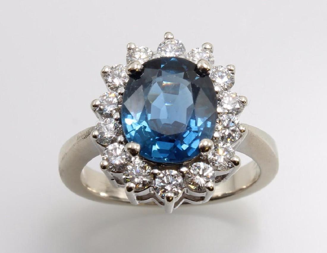 Blue Sapphire and Diamond 14K White Gold Ring: Features (1) 10 X 8 X 4.5mm oval blue Sapphire with worn facet junctions; surrounded by (14) round brilliant cut Diamonds, approx. .06ct each, Clarity: VS1 to SI1 Colour: I-J. Size 6 1/2. 6