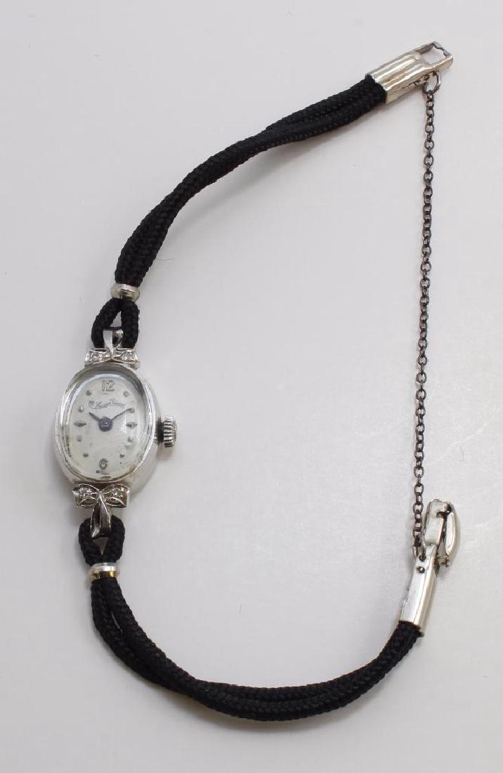 LADIES LUCIEN PICCARD WRIST WATCH. DIAMOND. 14K WHITE: 6 3/4" LONG. 29.5MM LUG END TO LUG END. FEATURES (4) SMALL ROUND ACCENT DIAMONDS. ARABIC NUMERALS AT 12 AND 6. 17 JEWELS. BLACK CORD BRACELET. 5.8GTW