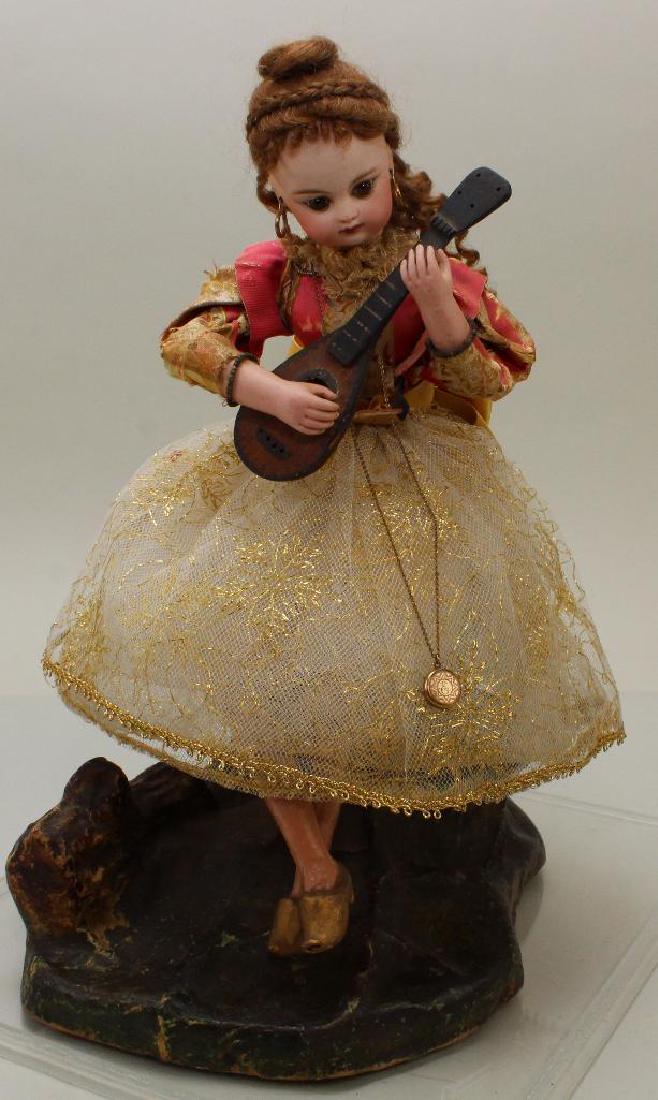 AUTOMATON: F.I.G. WOMAN PLAYING MANDOLIN.: This piece is activated when key is wound on back. Woman is sitting on a papier mache stump. Her head goes from side to side, right hand plays the mandolin and music plays. Overall hieght 13 1/2". Dol