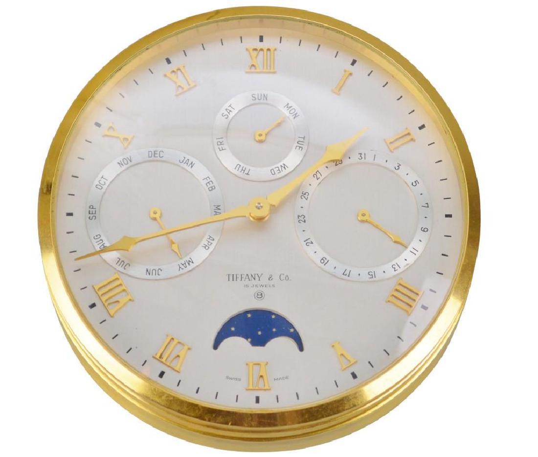 Tiffany and Co. Desk Clock: Gilt brass desk clock, has a 5". silvered dial with applied gilt brass. Roman hour numerals and hands. 4 sub dials for Day, Date, Month and Moon Phase. 15 Jewel, 8 day movement with alarm, monogrammed
