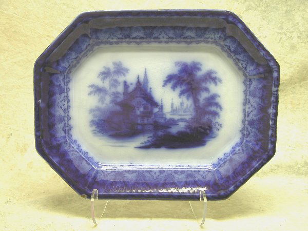 Flow Blue Platter.: Eight-sided platter with dark flow blue central landscape depicting Eastern buildings, trees and a bridge, border with foliage and scrolling decoration, 17 3/4" l., 14 1/4" d., 1 3/4" t., bottom mark,
