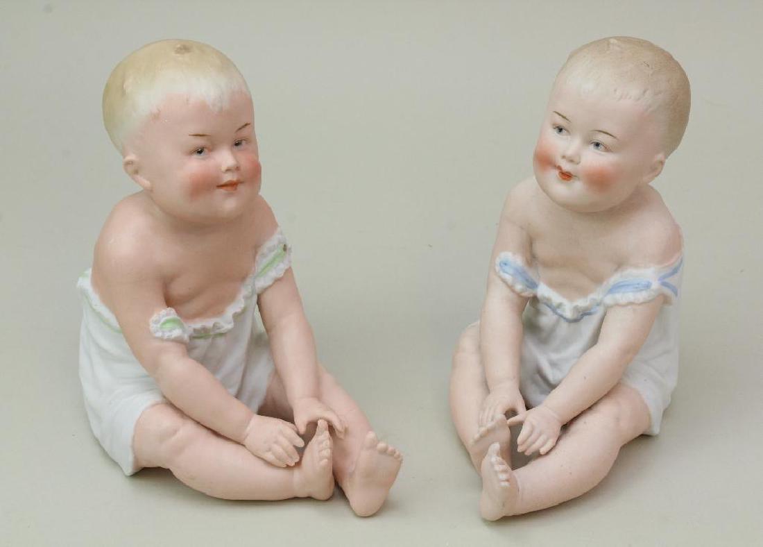 PAIR OF ANTIQUE HEUBACH PIANO BABIES.: 8 1/2" Similar sitting babies both marked with Heubach sunburst. (1) Is incised, the other printed Made in Germany and the incised mark. Their coloring is different as well as trim color on nightgown.