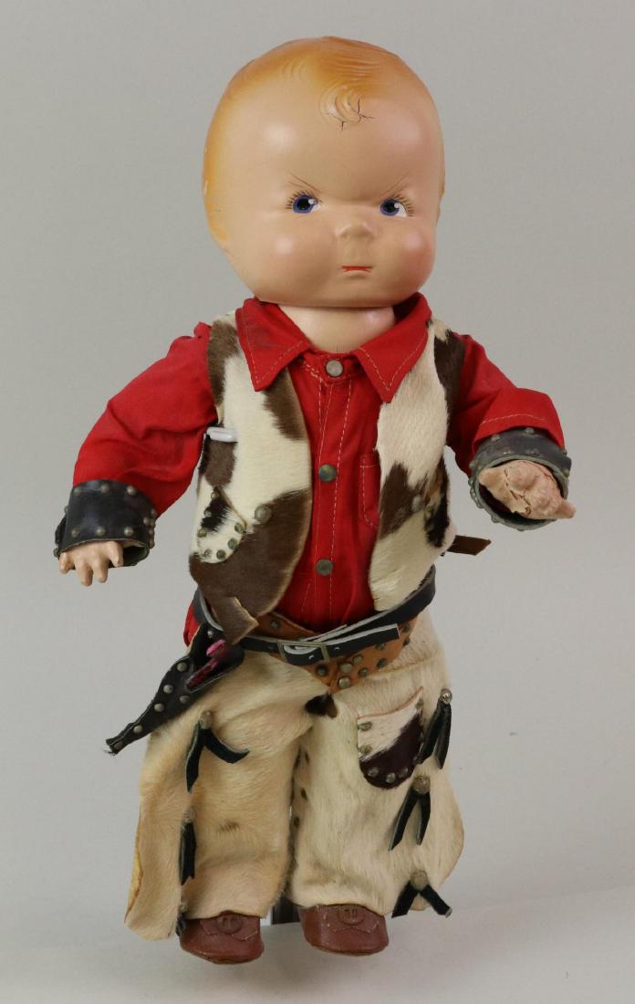 13" 1928 COMPOSITION AMERICAN CHARACTER "PUGGY" DOLL.: Doll is unmarked. Painted features (with frowning face), blonde hair. Dressed in original leather chaps, vest, holster. Oilcloth shoes. Stand. Condition: light crazing. Cracks on head in several place