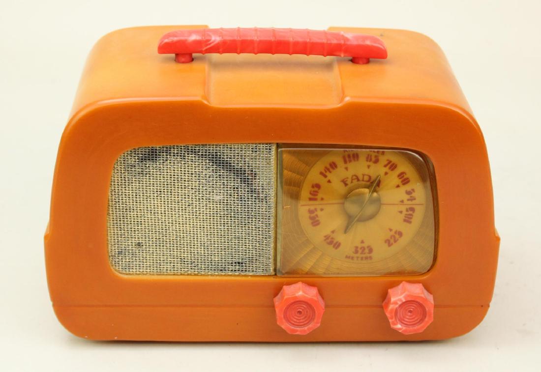 Fada Catalin Radio: Model 711. Dip top Fada radio. Butterscotch with red handle and knobs. Crack on bottom @ chassis mount point. Cord intact. Powers on. Dial lights. Dial shows some warping but tuning dial turns freely.