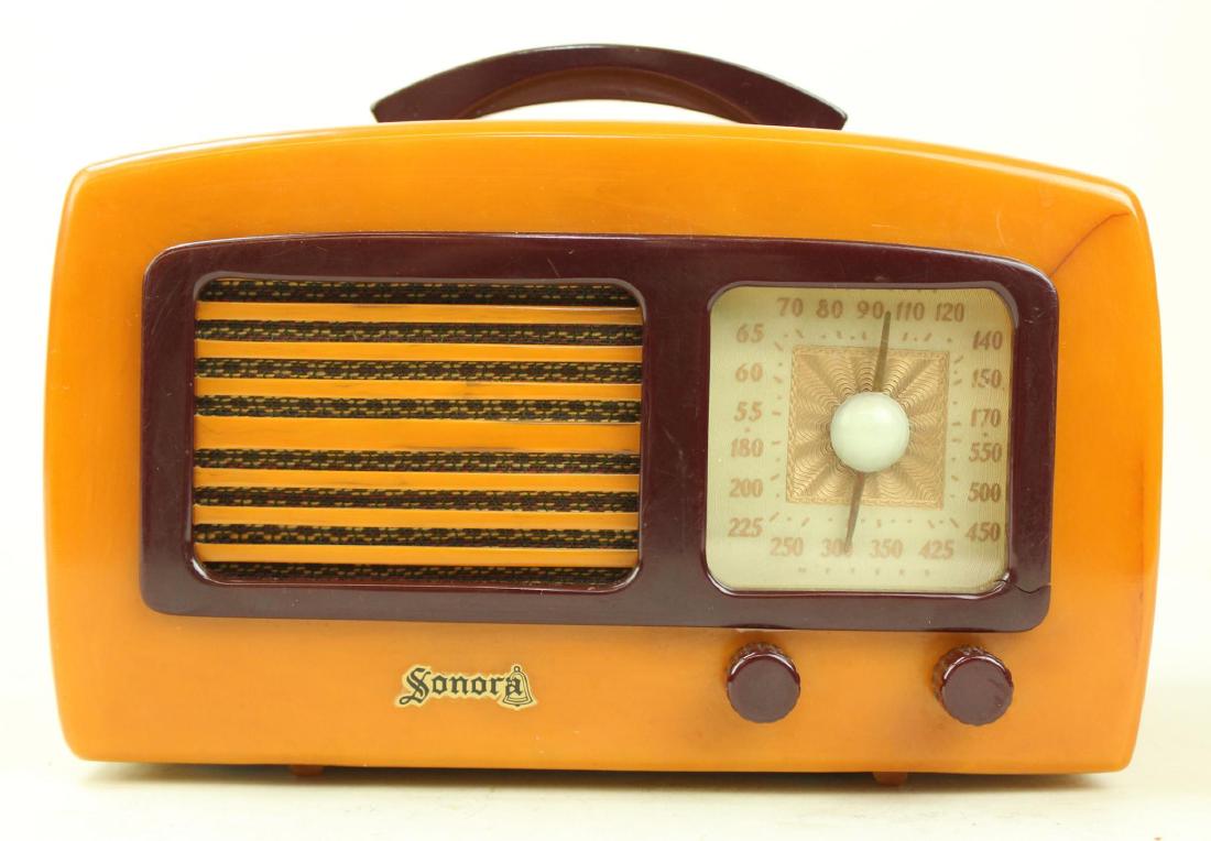 Sonora Catalin Radio: Model KM. c.1941. Originally alabaster but oxidized to yellow body with maroon grill, knobs and handle. Small 1" crack upper right of dial. Cord intact. Powers on.