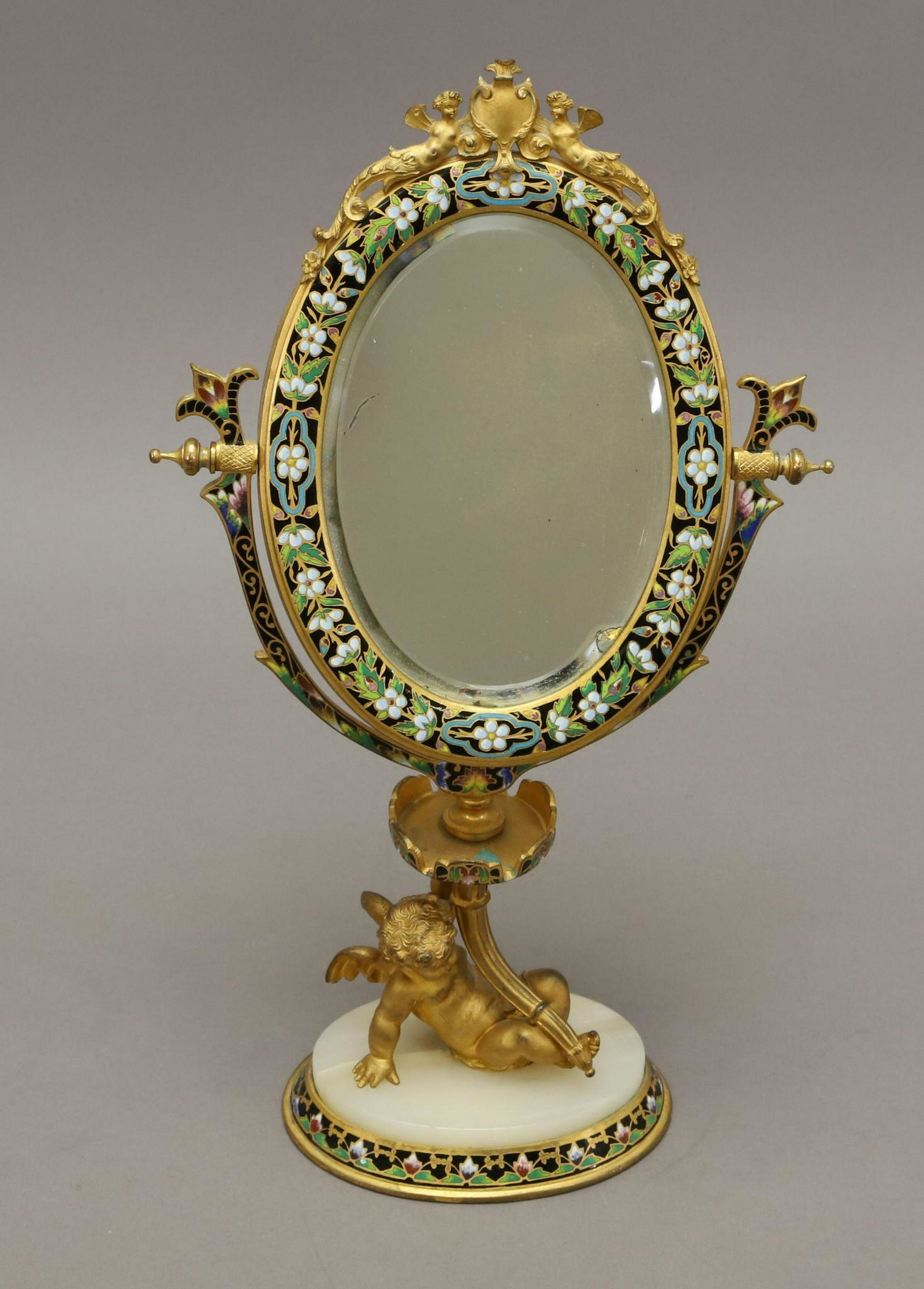 French Champleve Mirror: Hinged oval shaped mirror set on a cherub support with alabaster plinth, the top of the mirror surmounted by two ormolu winged female figures. 13"h x 8"w