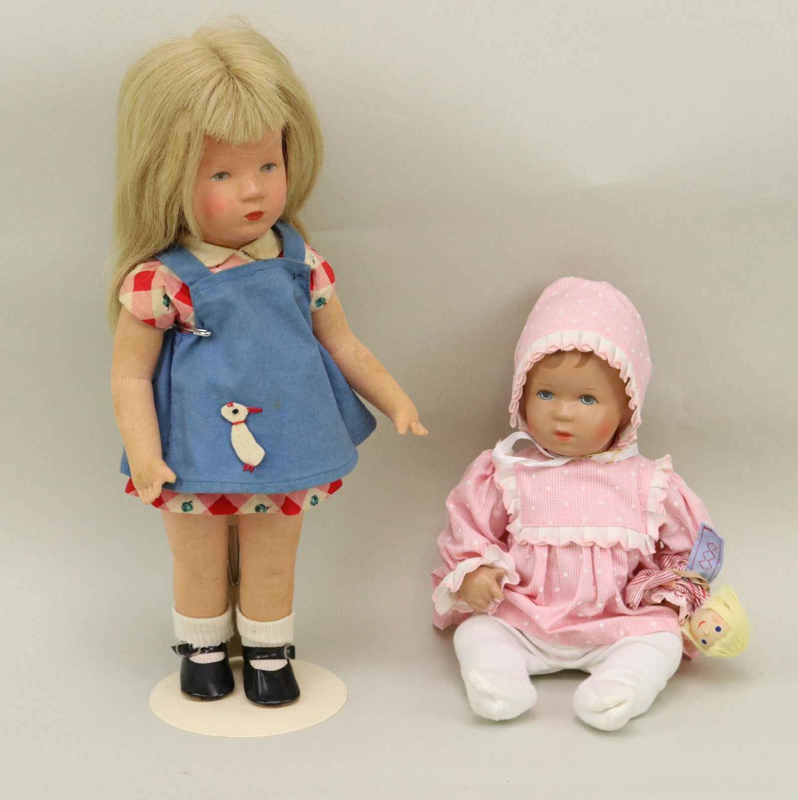 LOT OF 1950's-1970's DOLL(S).: Pair of Kathe Kruse dolls. Doll 1) 14" 1960-1975 with hard plastic head, pink muslin body, blonde human hair wig. Clothing/shoes may not be original. Stand. Condition: as stated. Face has rubs. Doll 2