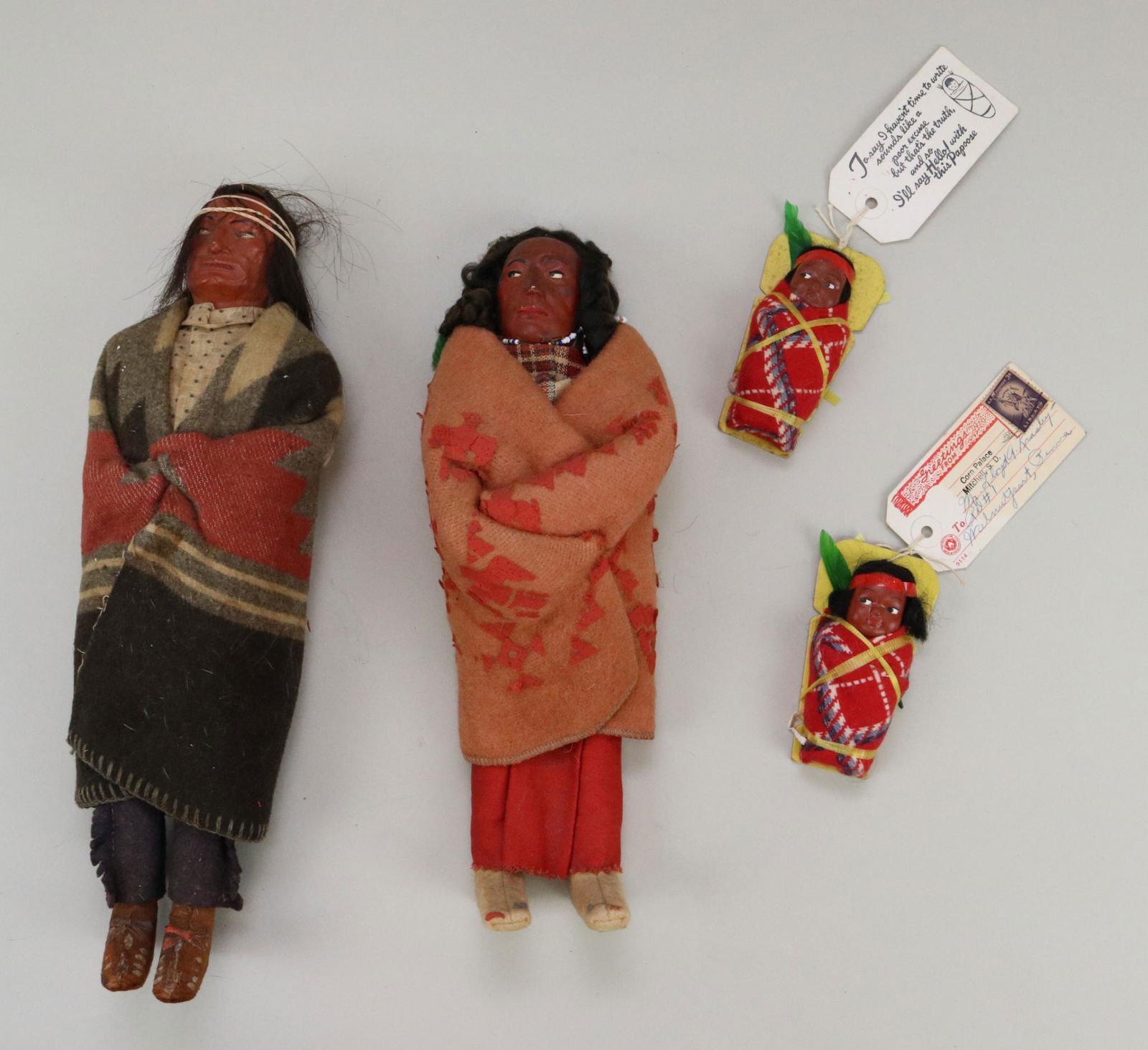 LOT OF NATIVE AMERICAN DOLL(S).: Lot of Skookum/type Indian dolls. 11 1/2" Female doll, 13 1/2" Male doll. Pair of 4" Papoose mailers marked: Created by American Indians. Corn Palace Mitchell, S.D. 1956 with 3 cent stamp on each. Con