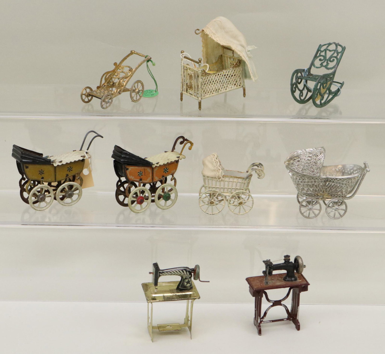LOT OF MINIATURES/DOLLS.: Lot of (9) metal miniatures. Pair of tin carriages with dolls Made in Germany. Tin sewing machine. Painted sewing machine. Pewter like carriage. German painted carriage. German painted doll bed, rocki