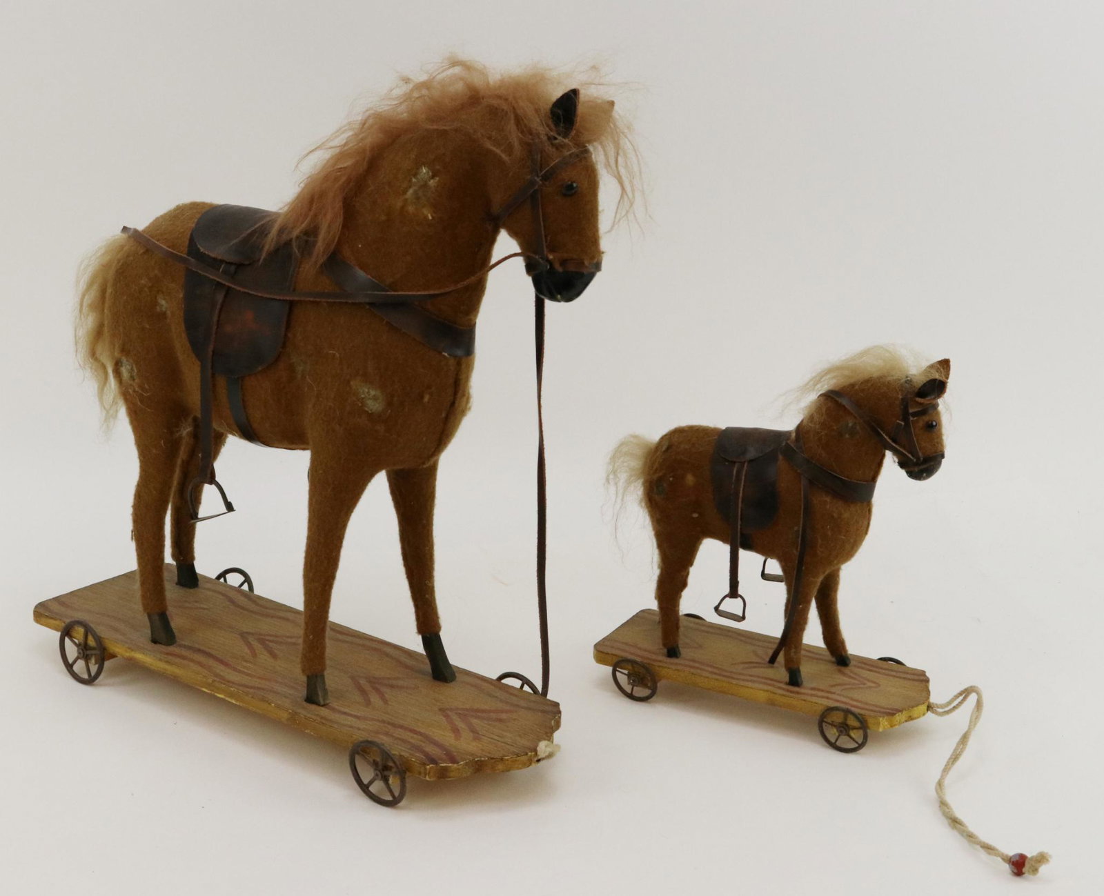 PAIR OF PLATFORM HORSES.: Pair of platform (reproduction?) horse pull toys. 9 1/2" T, 15" T. Both are covered in brown flannel, have brown glass eyes and leather tack. They stand on wooden platforms with metal wheels. Conditio