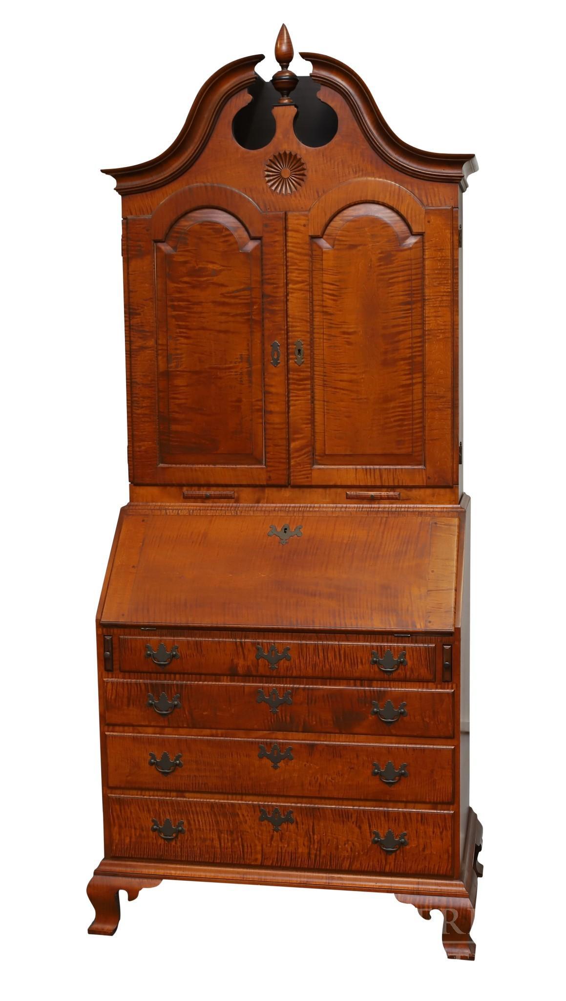 Eldred Wheeler Tiger Maple Secretary: Broken arch pediment with a turned cone finial, two arched doors to fitted interior and two slide out candle holders over a slant front desk with fitted interior over four graduated drawers on ogee br