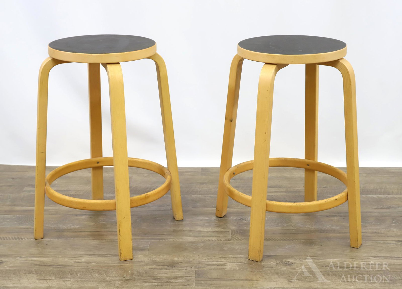 Pair of Alvar Aalto for Artek Stools: (2) Bentwood birch L-shaped legged stools with oval black linoleum top. 26"h