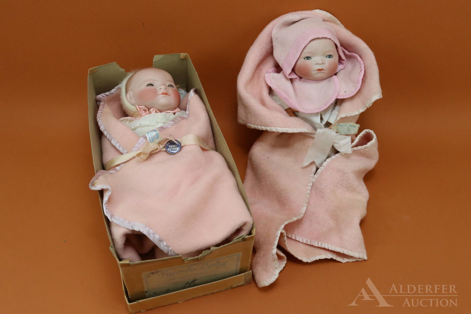LOT OF GERMAN BISQUE HEAD BABY DOLLS.: Pair of GRACE S. PUTNAM "BYE-LO" Babies. Both dolls have blue sleep eyes, painted dark blonde hair, cloth "frog" bodies, celluloid hands. They are both wrapped in tagged pink flannel George Borgedlt b