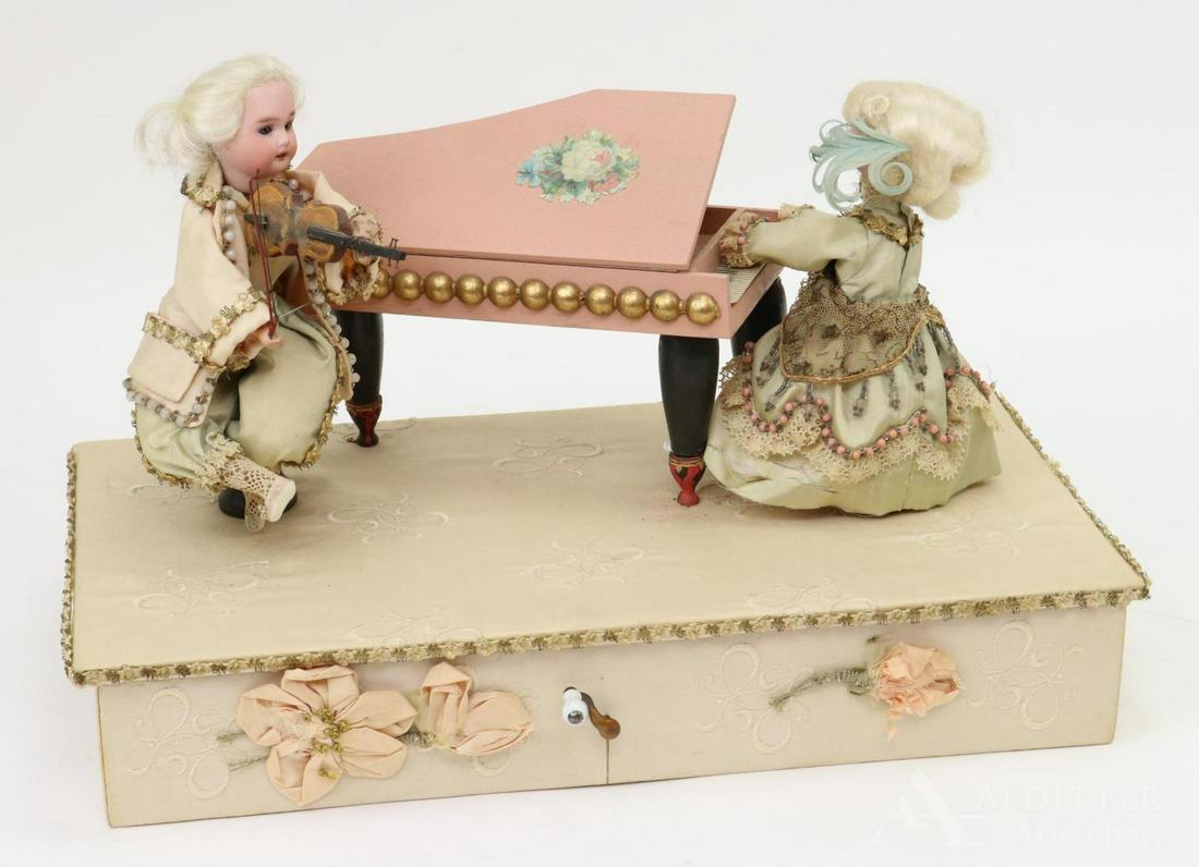 AUTOMATON: Unmarked Two - Doll Mechanical. Two 7"- 8" (probably) German bisque head dolls on a base that measures 15 1/2" L x 8 1/4" W x 3" T. (Overall height is 10".) The lady doll sits at a piano and the boy s