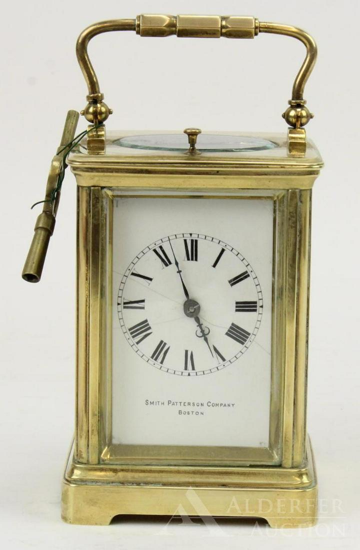 French Carriage Clock: Polished brass carriage clock, retailed by Smith Patterson Company of Boston, with beveled glass panels and enamel dial decorated with Roman numerals. Without handle, item measures 4.75" h.