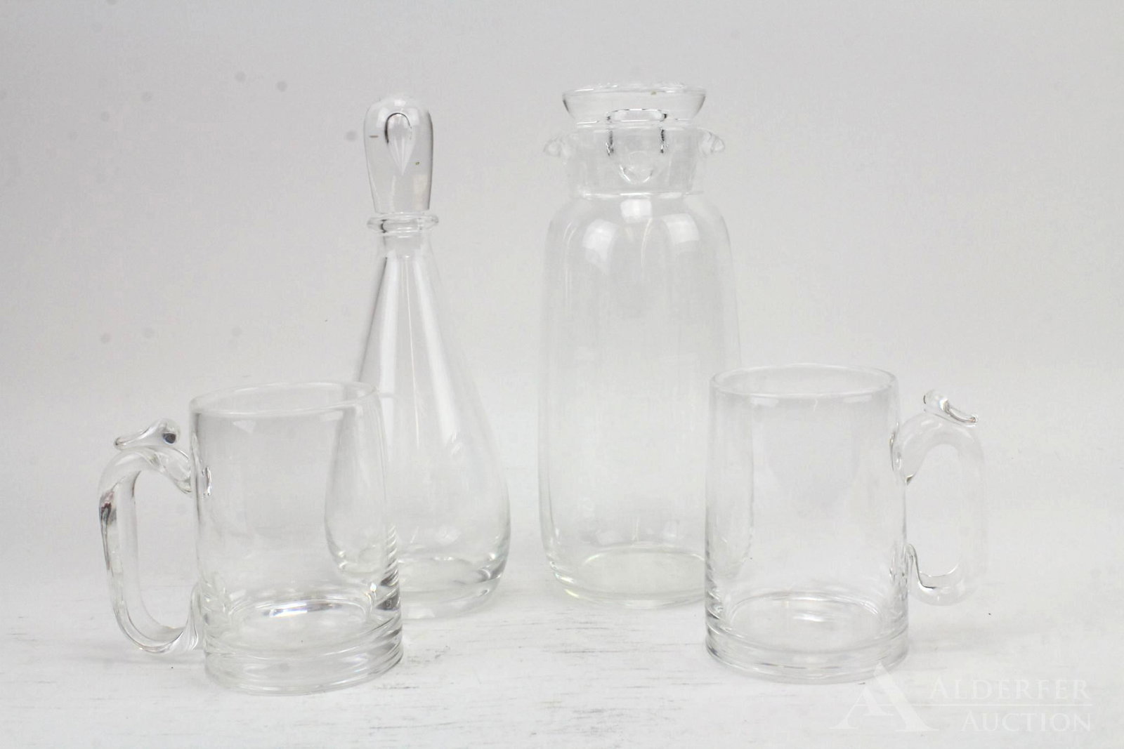 Steuben Glass Beverage Set: Steuben glass grouping includes double notched carafe (10"), decanter with teardrop stopper and a pair of mugs with applied glass thumb rests (4.75"h).