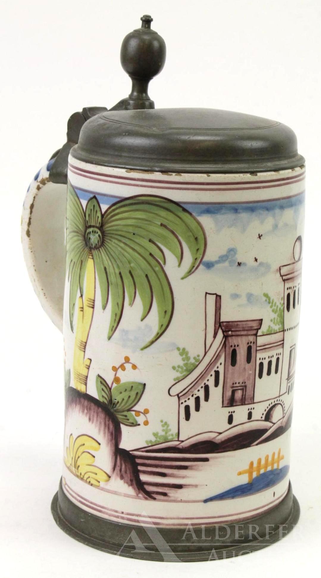 German Faience Pewter Mounted Tankard: A tin-glazed earthenware tankard in columnar form, with polychrome decoration and pewter cover with thumb rest knob. Tropical landscape with building. Minor flaking and chips in glaze on rim and handl