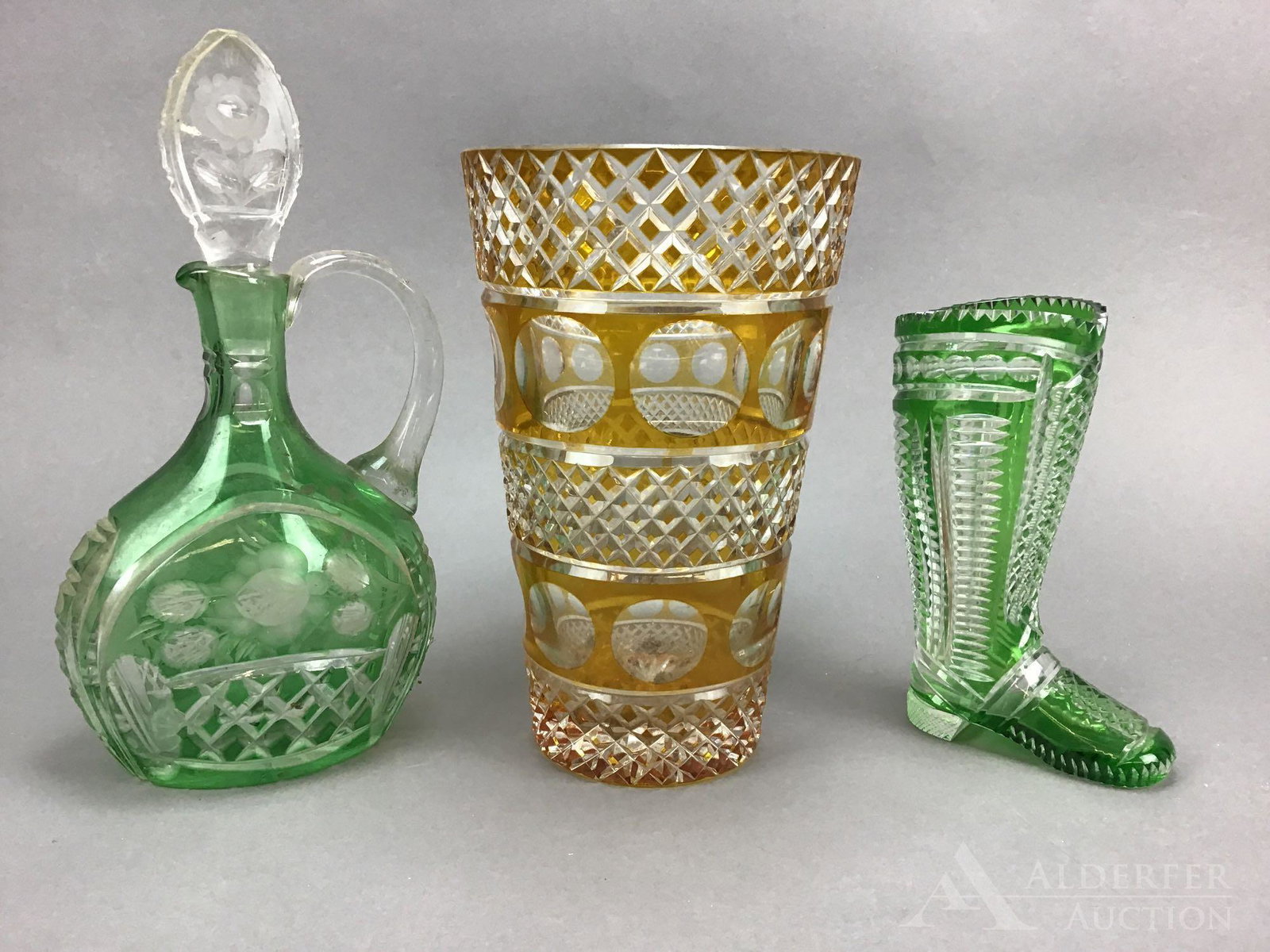 Bohemian Crystal Grouping: Cut to clear glass grouping including a green boot measuring 8” h, a green cruet/decanter with stopper measuring 12” h, and an amber vase measuring 10”h.
