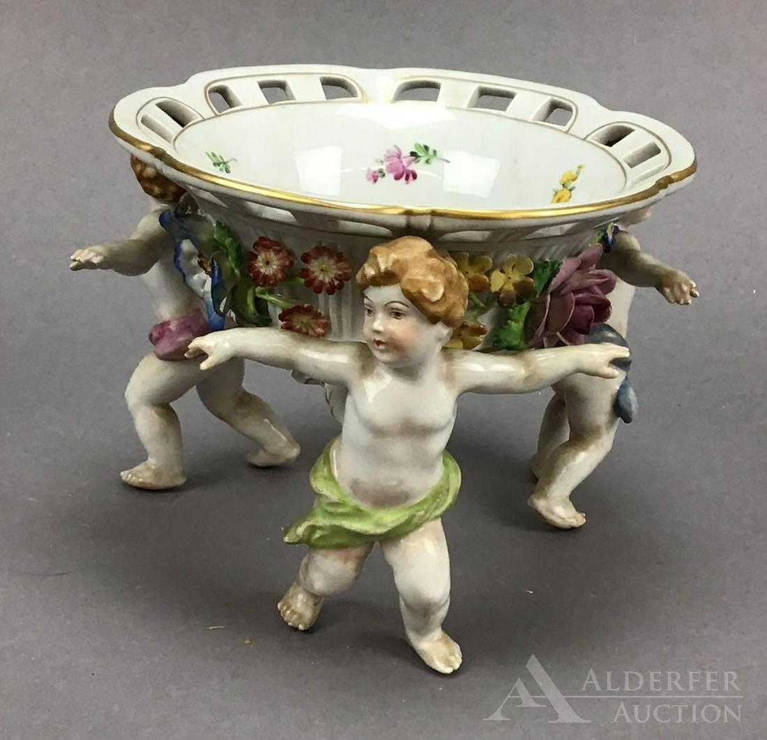 Schierholz Porcelain Bowl: Schierholz (Germany) footed figural bowl, featuring dancing putti and florals, with reticulated top and gilt rim. Measures 5.25”h. Damage to one of the putti's fingers.