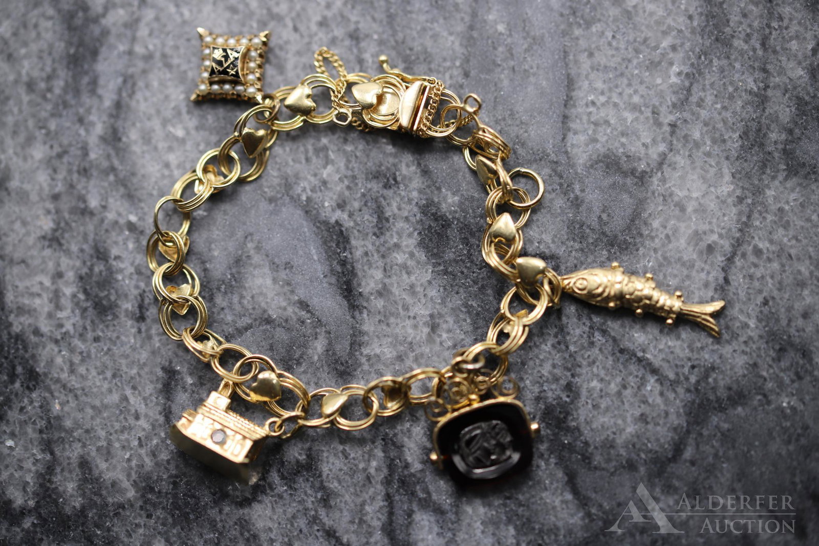 14KY Gold Charm Bracelet: Including 10KY Fraternity Pin with seed Pearls, 14KY Church, Gold plated Carnelian fob spinner with carved double Roman profile, 10KY articulated Fish. 7" long link bracelet with heart stations. 12.