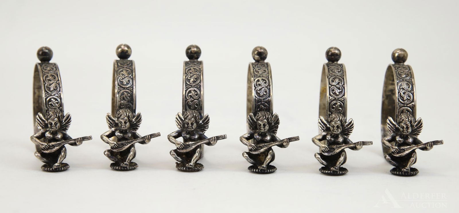 .800 Silver Napkin Ring Place Card Holders: Grouping of (6) .800 silver napkin rings decorated with a cherub playing a lute adorned with a place card holder finial. 2"h x 2.5"d and 4.38ozt