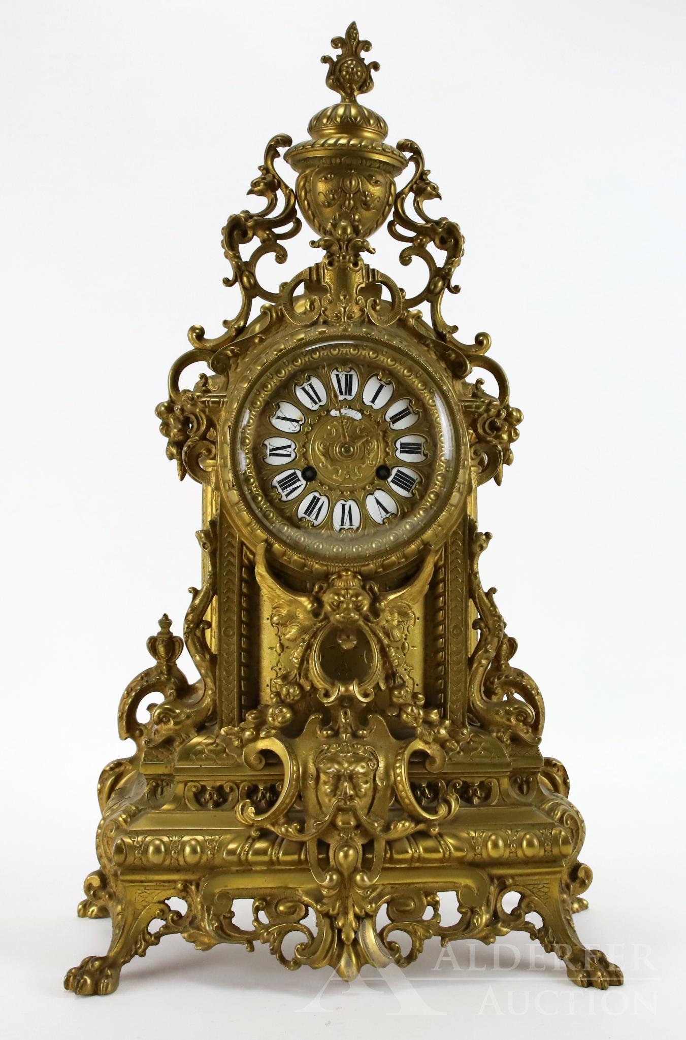 Louis XIV Mantle Clock: Elaborate bronze 8-day clock with Roman numeral clock face. Urn shaped finial and scrollwork throughout. Applied decoration includes winged lion, dolphins and male's face. Rectangular base ends in paw