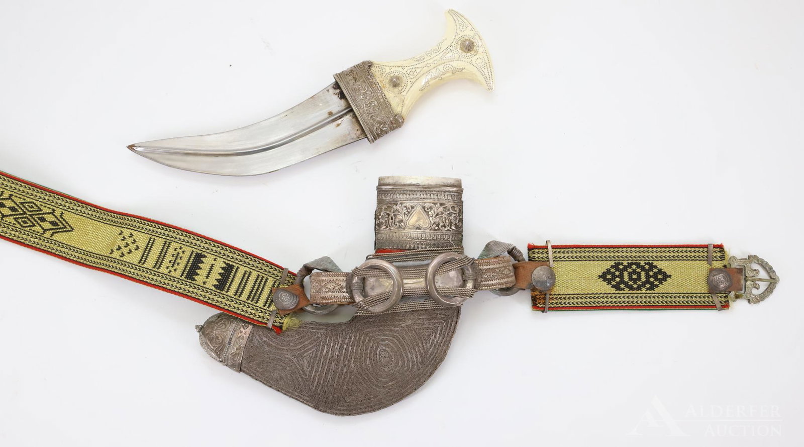 20th Century Middle Eastern Jambiya Dagger: Middle Eastern Jambiya dagger with bone grip decorated with silver pin work. Scabbard presents silver thread work and is mounted on decorative belt. Dagger measures 11" (6.75" blade) with areas of sca