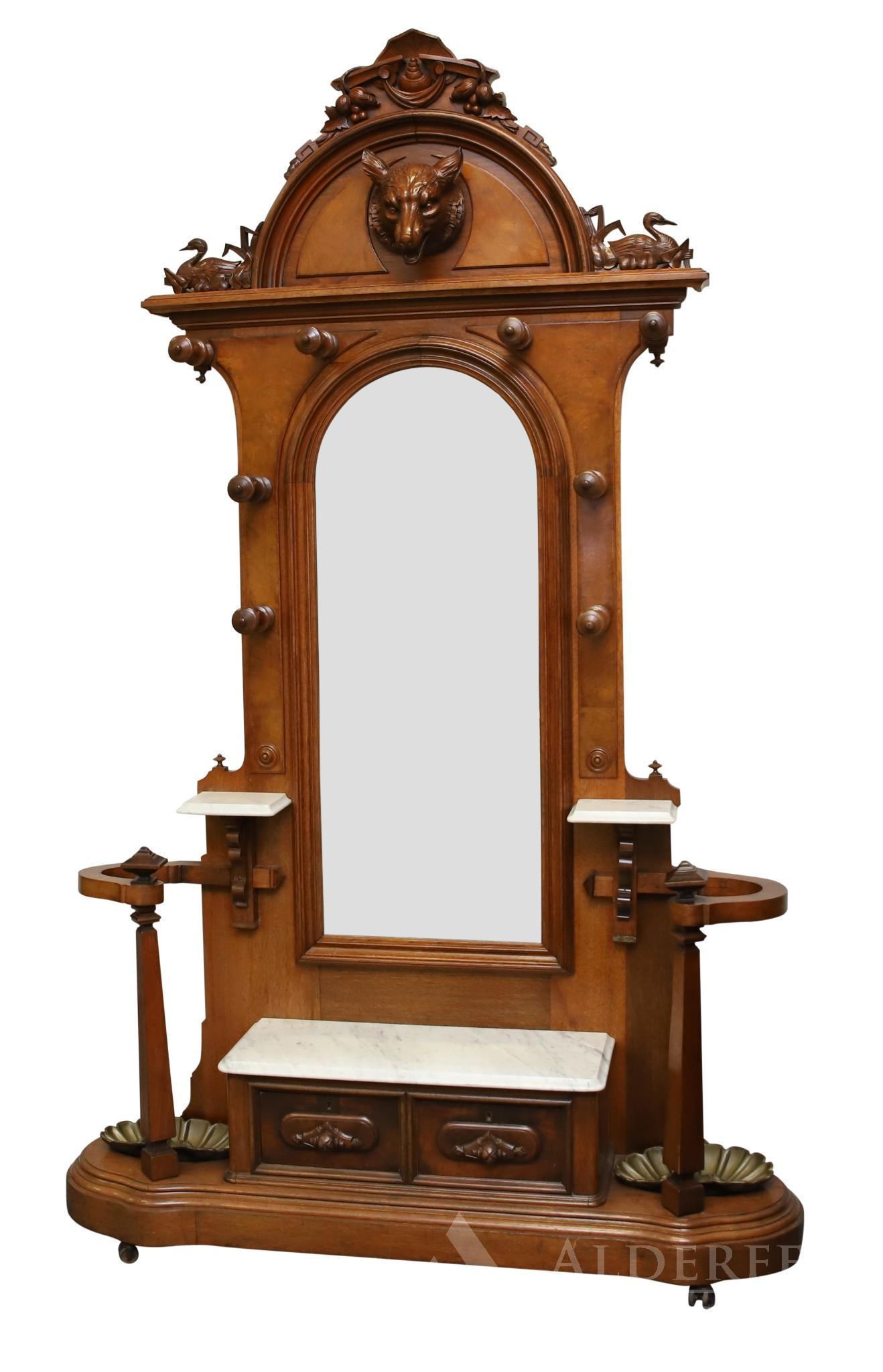 Victorian Eastlake Walnut Hall Tree: Arched top with wolf's head and mallard carved motifs, arched mirror, eight hanging pegs, marble top gloves drawers, and two umbrella stands with brass shell inserts. 104h" x 60w" x 16d"