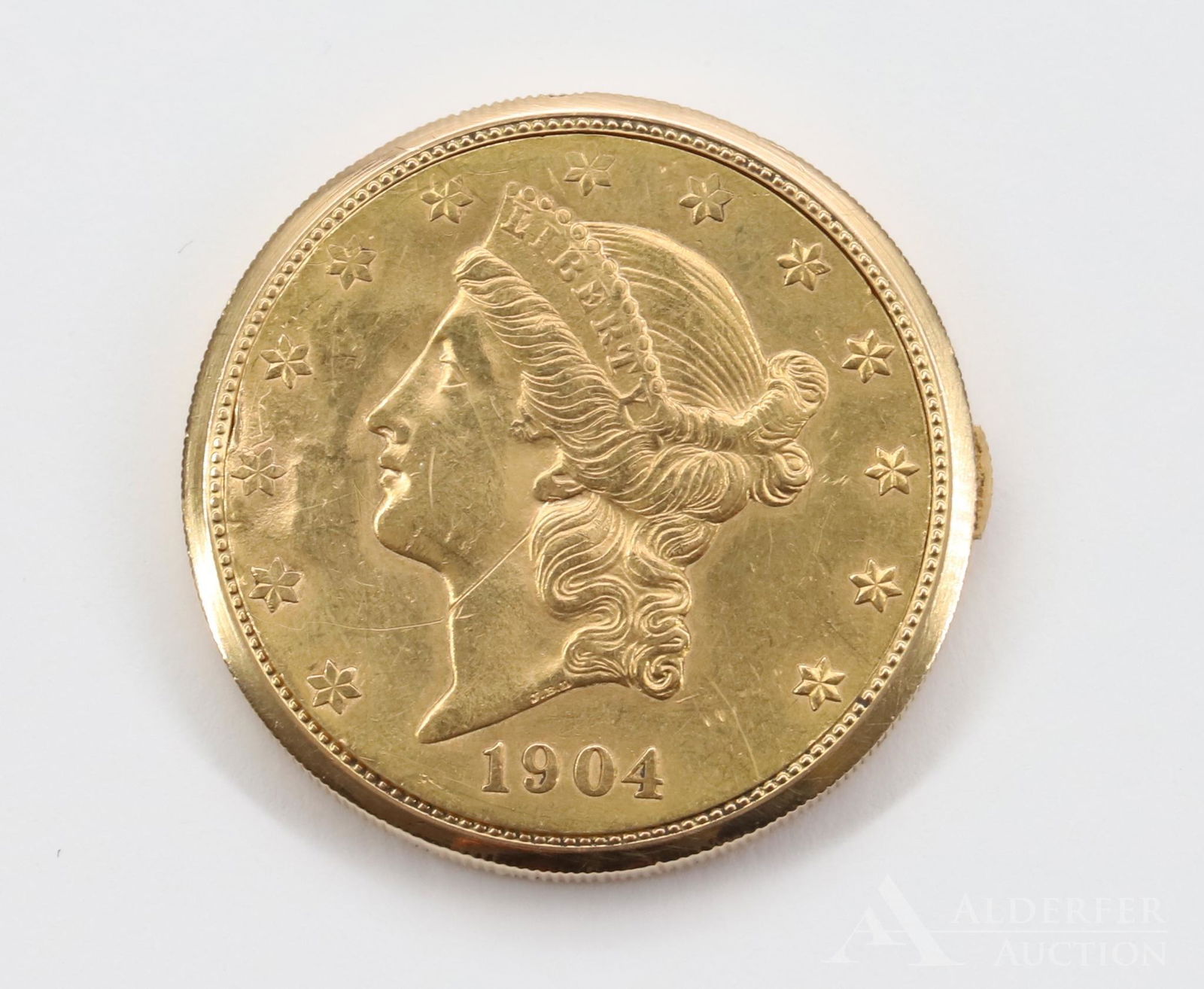Juvenia 18KY Watch in Coin Setting: Bezel set Liberty Head 1904 United States of America twenty dollars coin shell. Bezel with built in button release features an 18KY gold swing out timepiece by Juvenia. Rippling of coin near hinge. M