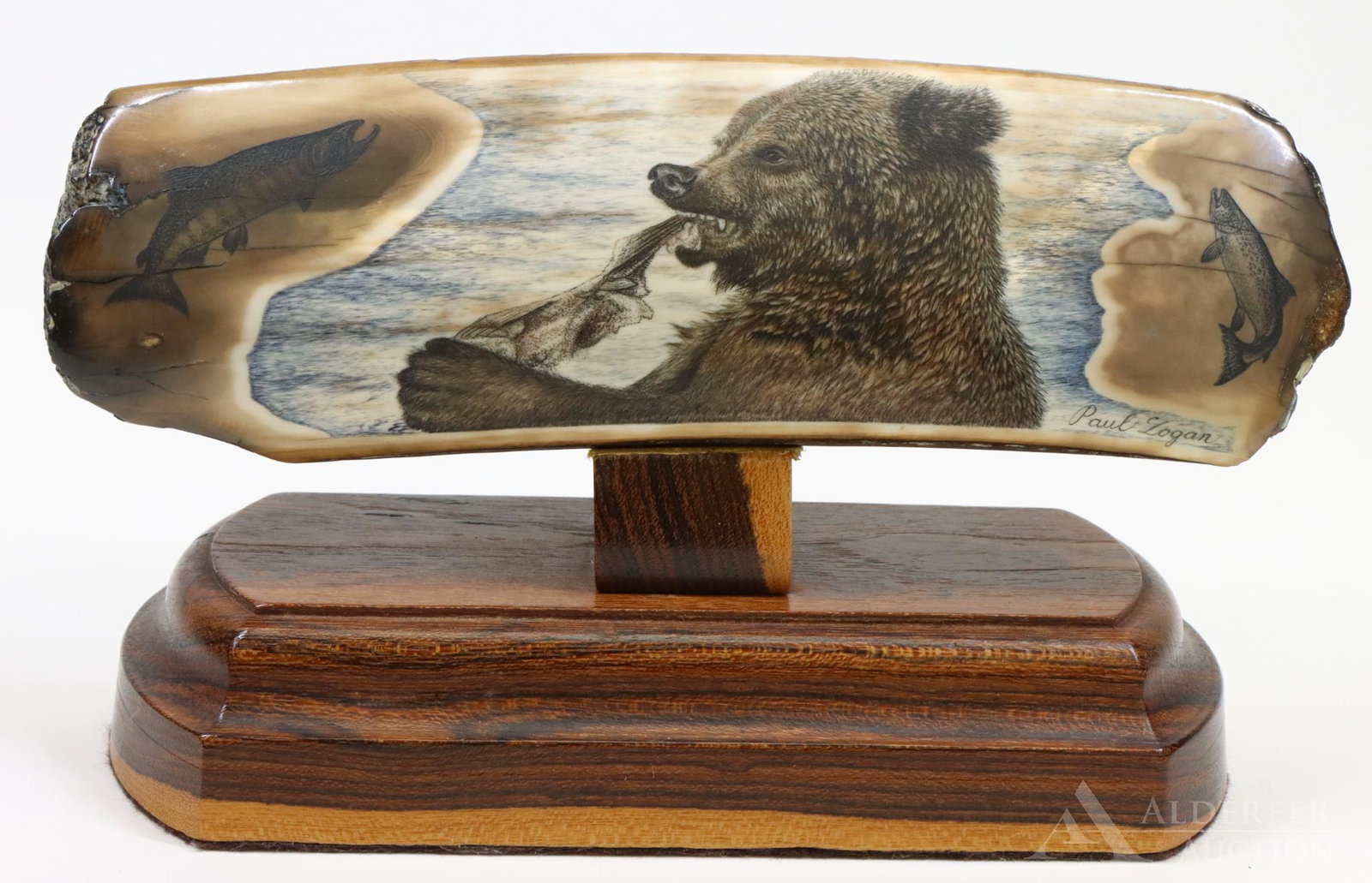 Paul Logan Walrus Ivory Scrimshaw: Paul Logan artist signed Fossil Walrus Ivory Scrimshaw Carving of Bear with fish, on wood base, with Eskimo Artifact sticker. 2.25"h x 7"w without base