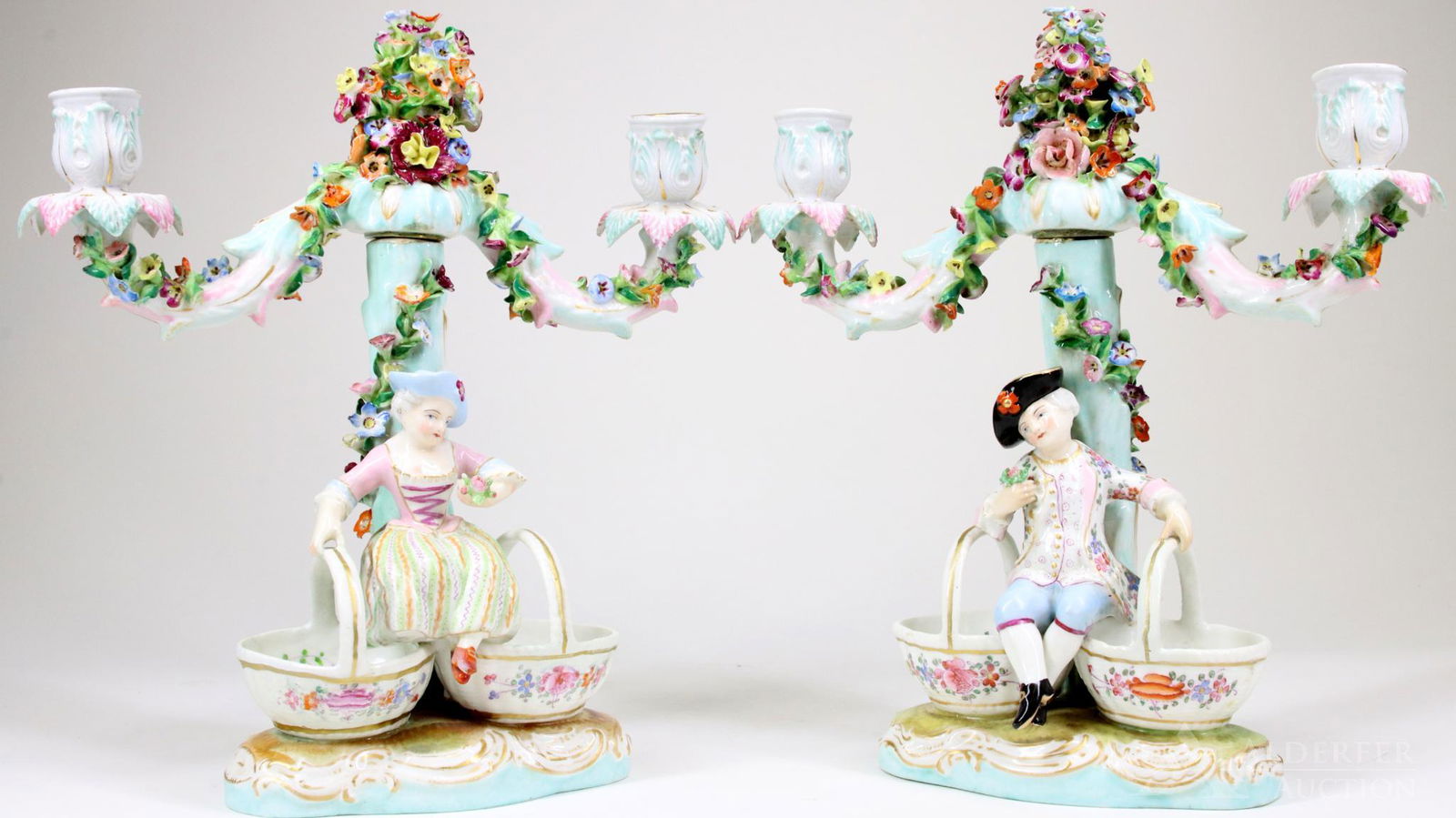 Meissen Figural Candlesticks: Meissen Figural Double Arm Candlesticks of Man and Woman with Baskets, adorned with multi-colored applied flowers on pale turquoise. Under glaze blue crossed swords mark. 10.25"h x 9.5"w