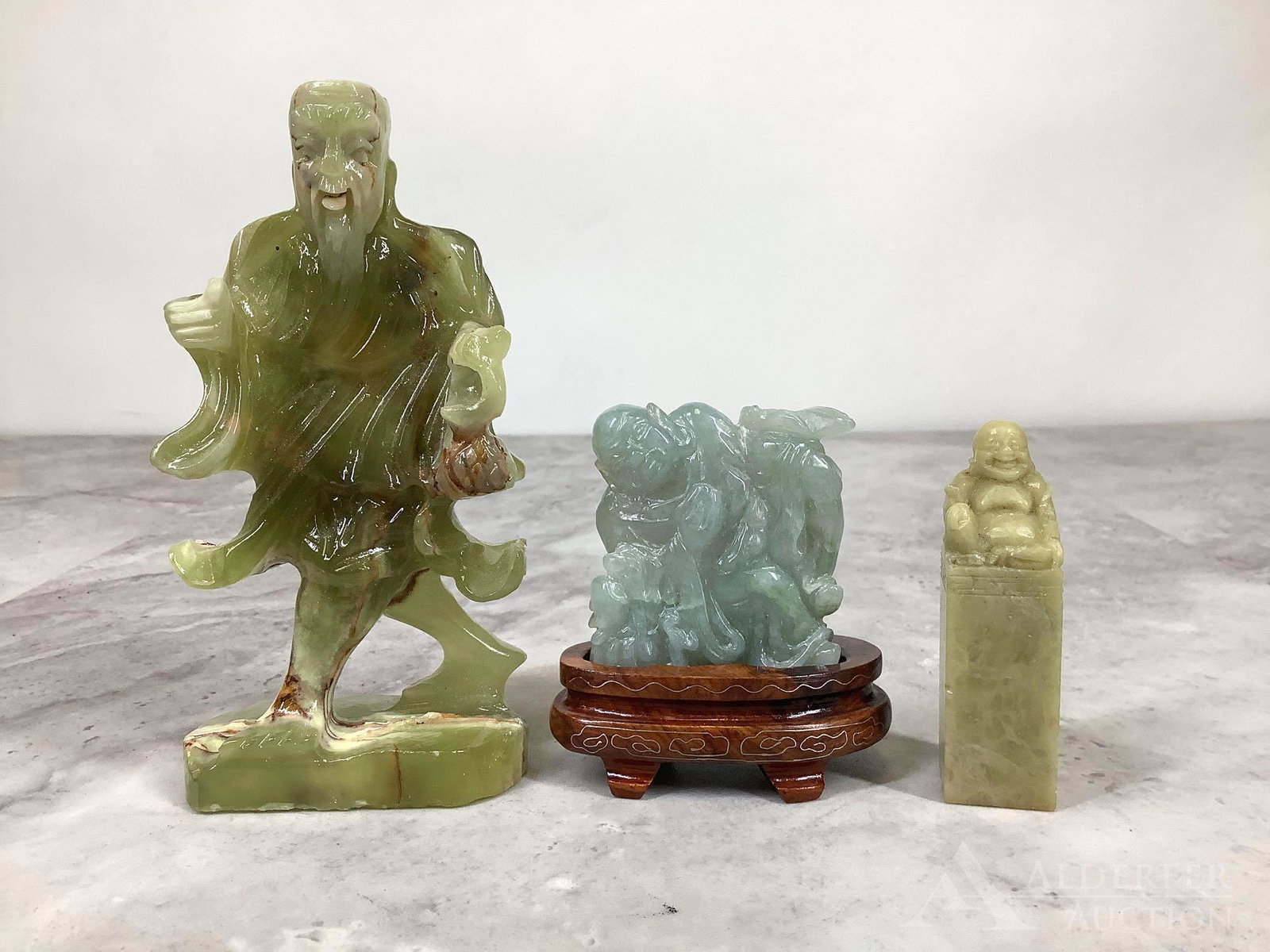 Carved Stone Sculptures & Seal: Green stone carvings (3), including Shou, resting Buddha, and laughing Buddha seal. Shou is missing some elements. Resring Buddha has a stand. Shou is 5"h x 2.5"w x 1.5"d