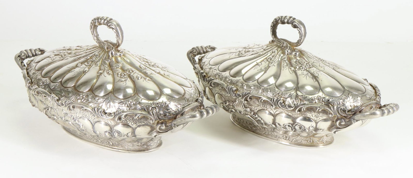 Kirk Sterling Silver Vegetable Servers: Early 20th century pair of covered oval repousse servers with reeding, elaborate scroll and floral decoration surrounding cartouches, scalloped edges, foliate double handles to the bodies and round ha