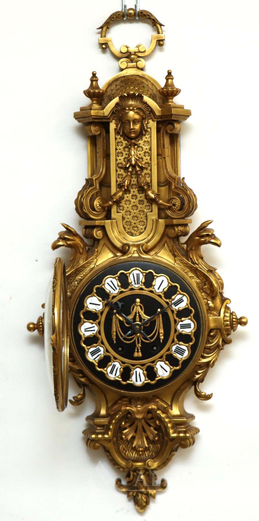 Tiffany Cartel Clock: Rococo Revival ormolu pendulum clock, the face featuring enamel Roman numeral dial set in an architectural frame with central swag applied over ebony wood, behind a dome glass door, framed by a bud dr