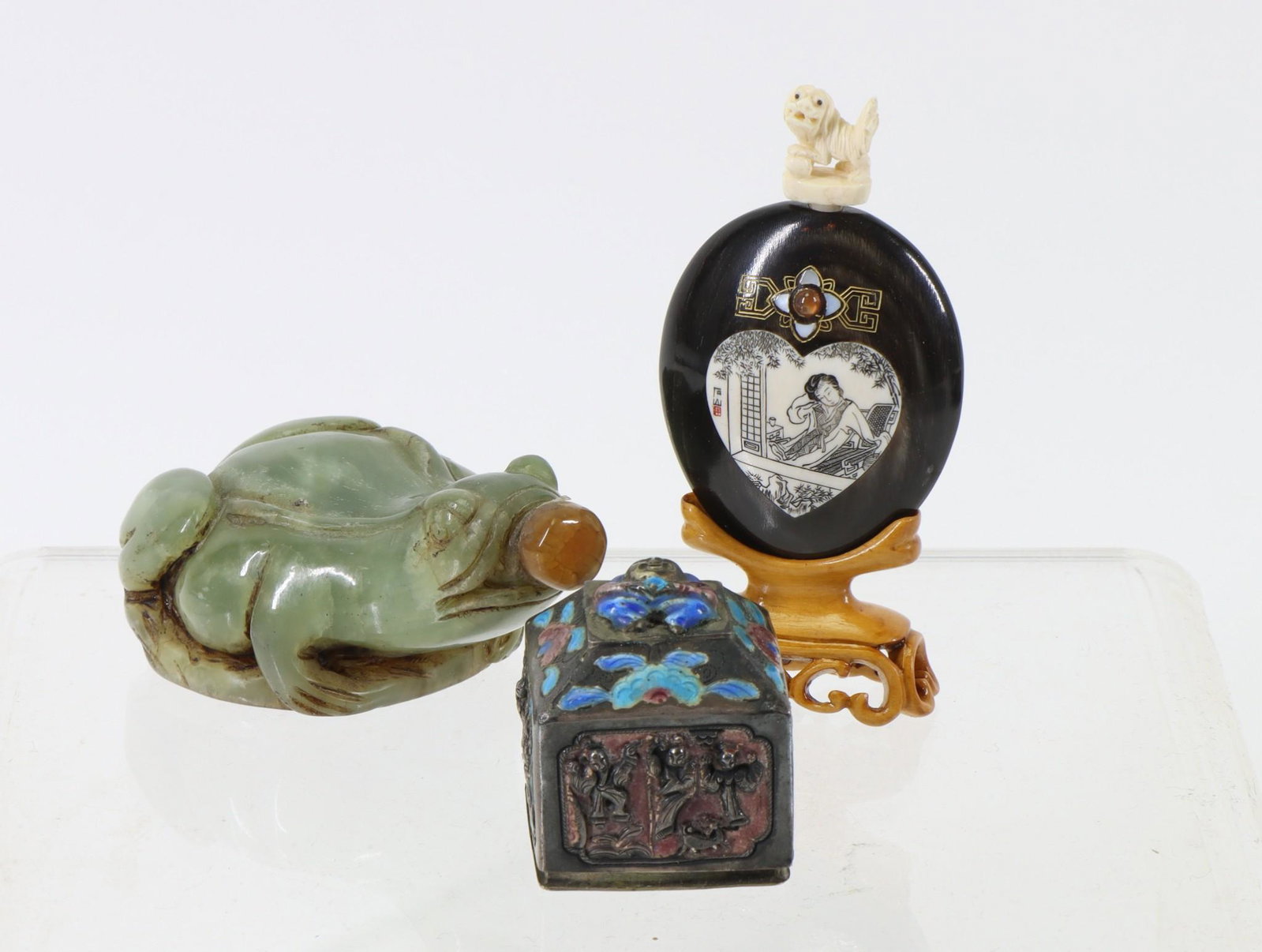 Chinese Snuff Bottles: Carved green stone frog form bottle, carved horn and bone bottle with reclining lady, foo dog spoon, and script, and an unmarked enamel silver box with figure, flowers, and script. The frog is missing