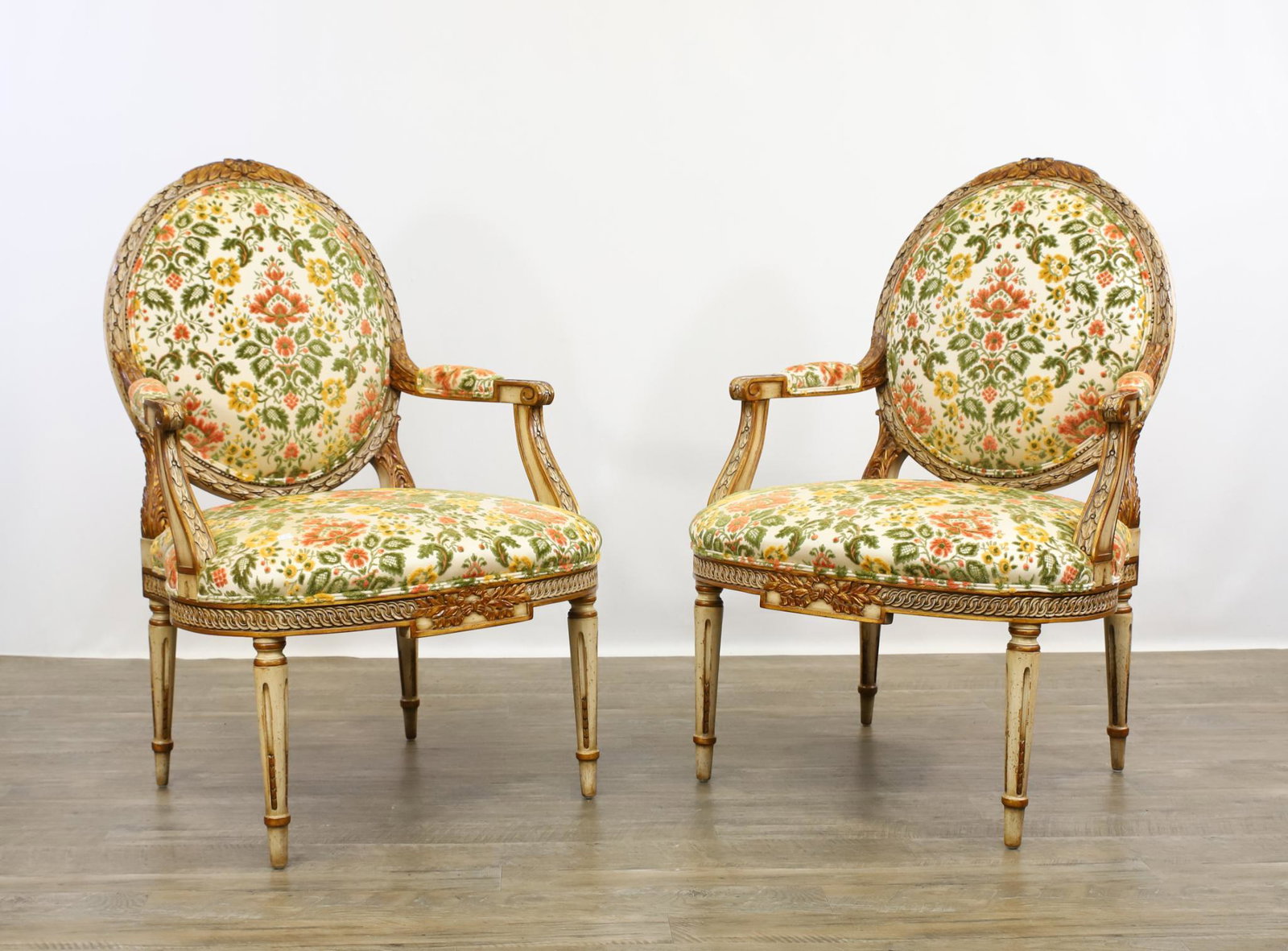 Karges "Louis XVI" Fauteuils: Pair of fauteuils, parcel gilt with antiqued white finish, foliate decoration throughout, with scroll arms, fluted tapered legs, and floral upholstery. 40"h x 27"w x 23"d, seat height 17.5" **Please N