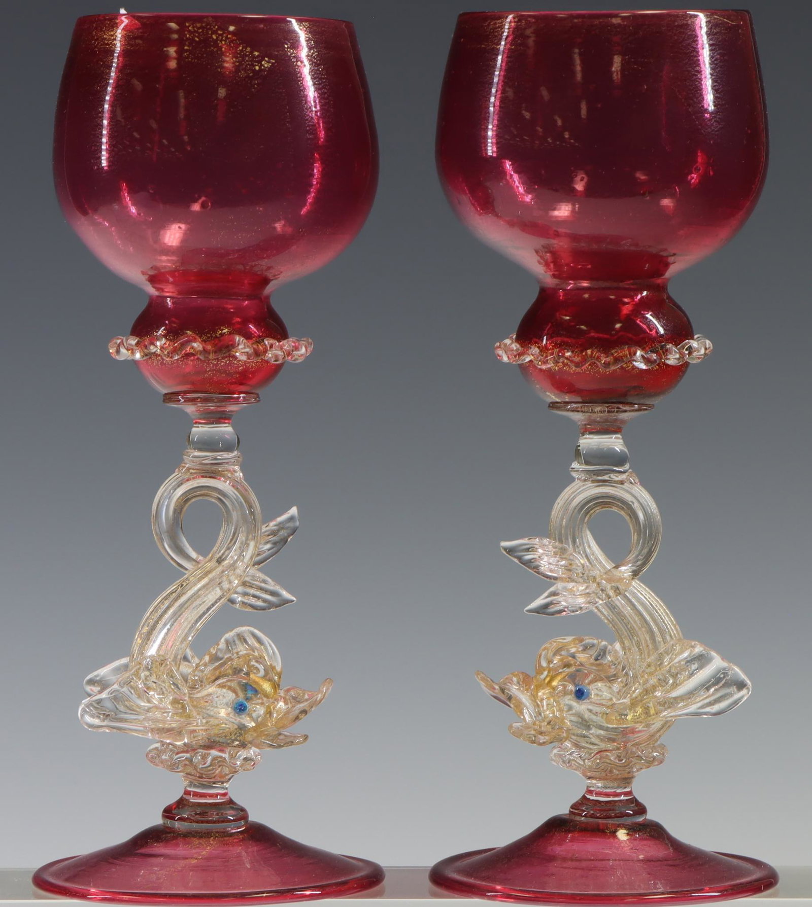 Murano Art Glass Dolphin Wine Glasses: Italian blown glass wine glasses (2) with ruby bowls and feet, dolphin form stems, and gold aventurine throughout. 7.5”h x 3”w **Please Note: This item is NOT eligible for in-house shippin