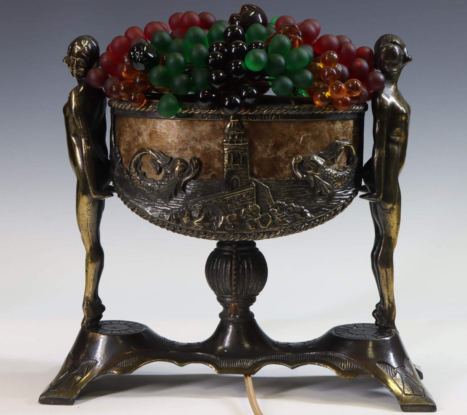 Art Deco Fruit Basket Lamp: Czechoslovakian Art Deco faux bronze and mica lamp with nude females supporting the basket decorated with towers and dolphins, with removable colored glass fruit and light. Turns on. 12"h x 12"w x 4.5