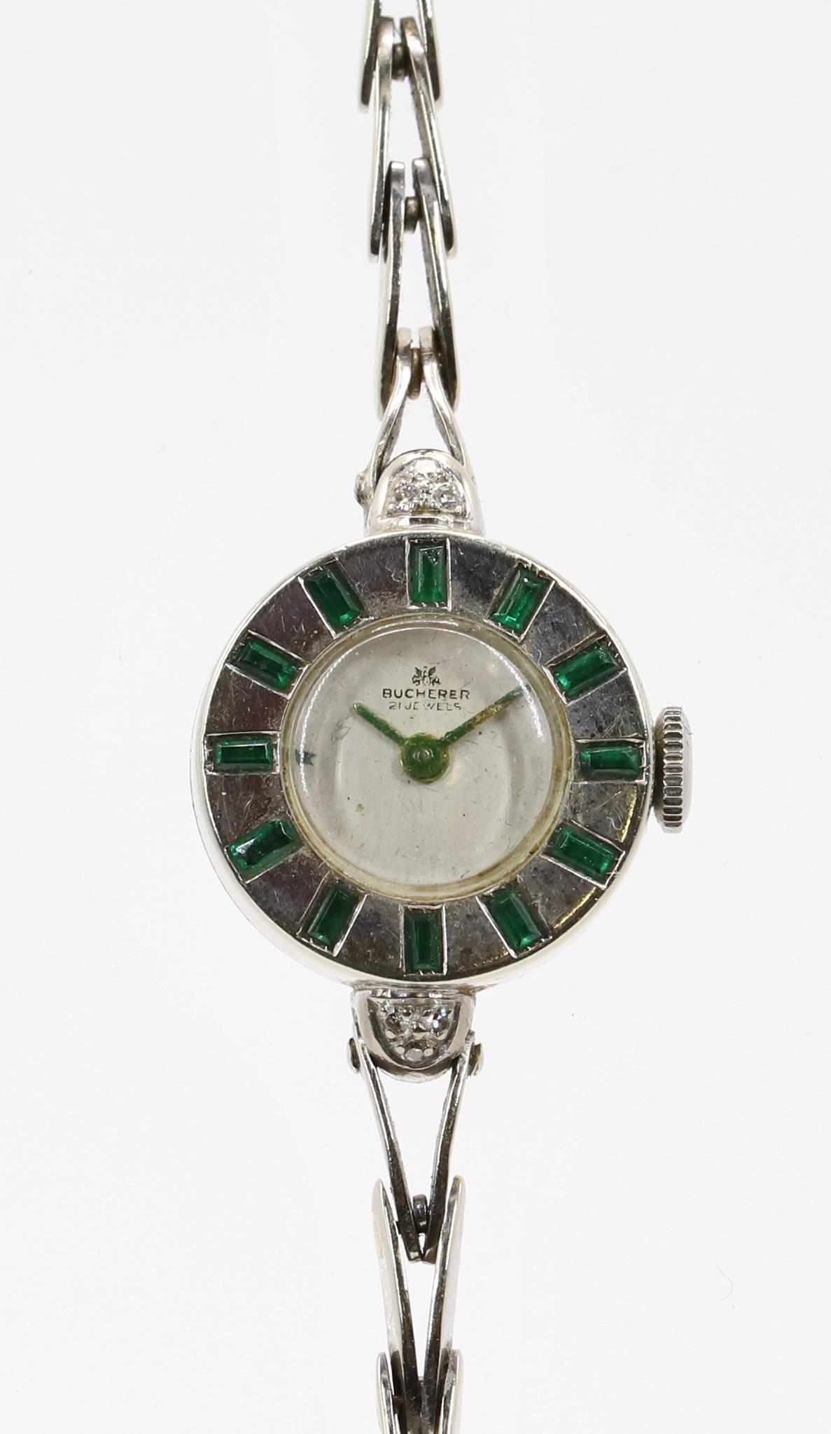 Bucherer 18KW Gold Emerald Diamond Wrist Watch: Bucherer ladies wrist watch features rays of emerald baguettes in an 18kw gold round case, 17.5mm diameter with (3) round diamond accents at each lug end. 21 jewels. "V" link bracelet is 14kw gold. Cu