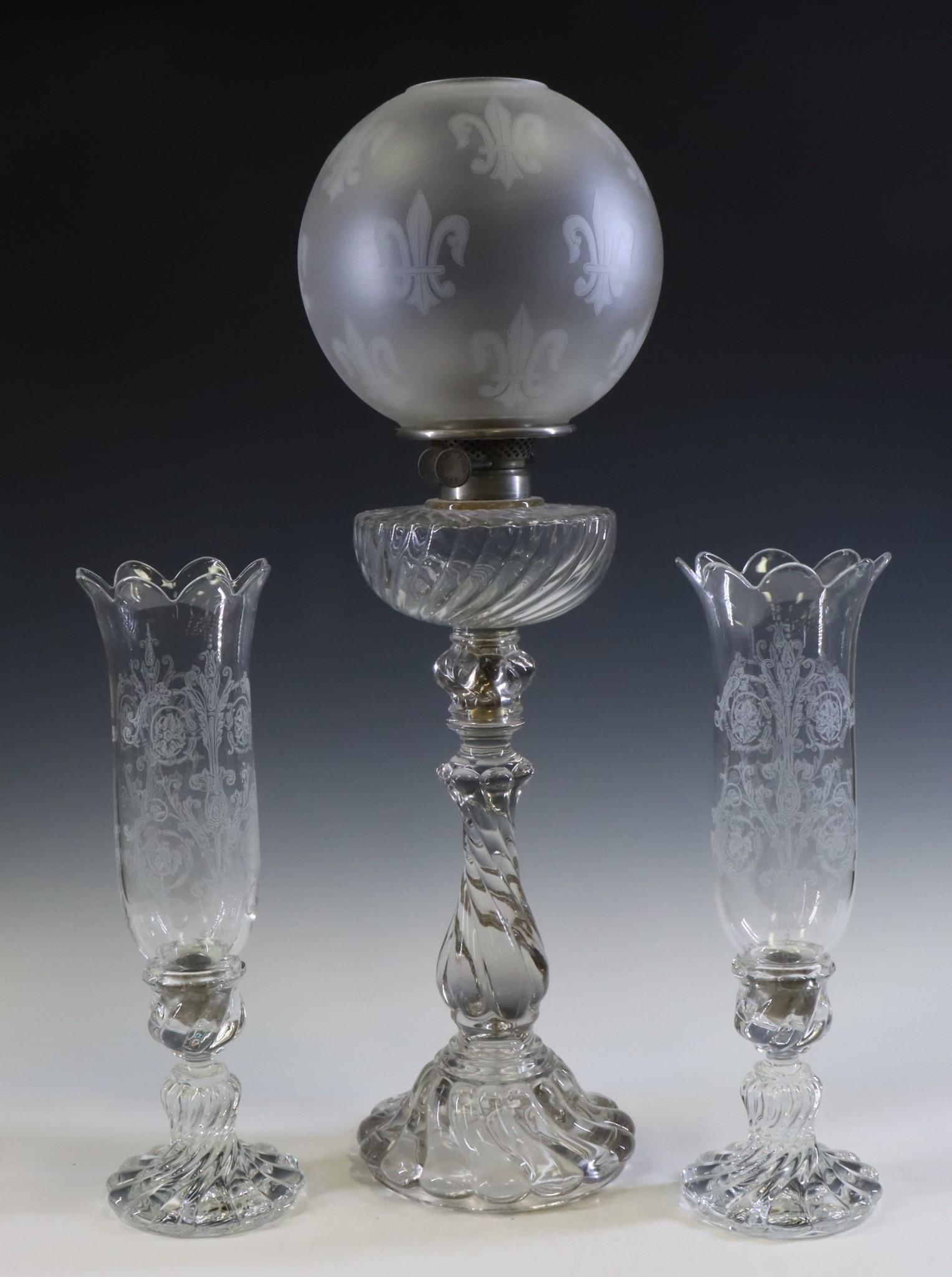 Baccarat Oil Lamp & Candlesticks: Baccarat whale oil lamp with twisted base and frosted fleur-de-lis globe. Accompanied by a pair of candlesticks, also of twisted form, with swag etched globes. 27.5"h and 16"h **Please Note: This item