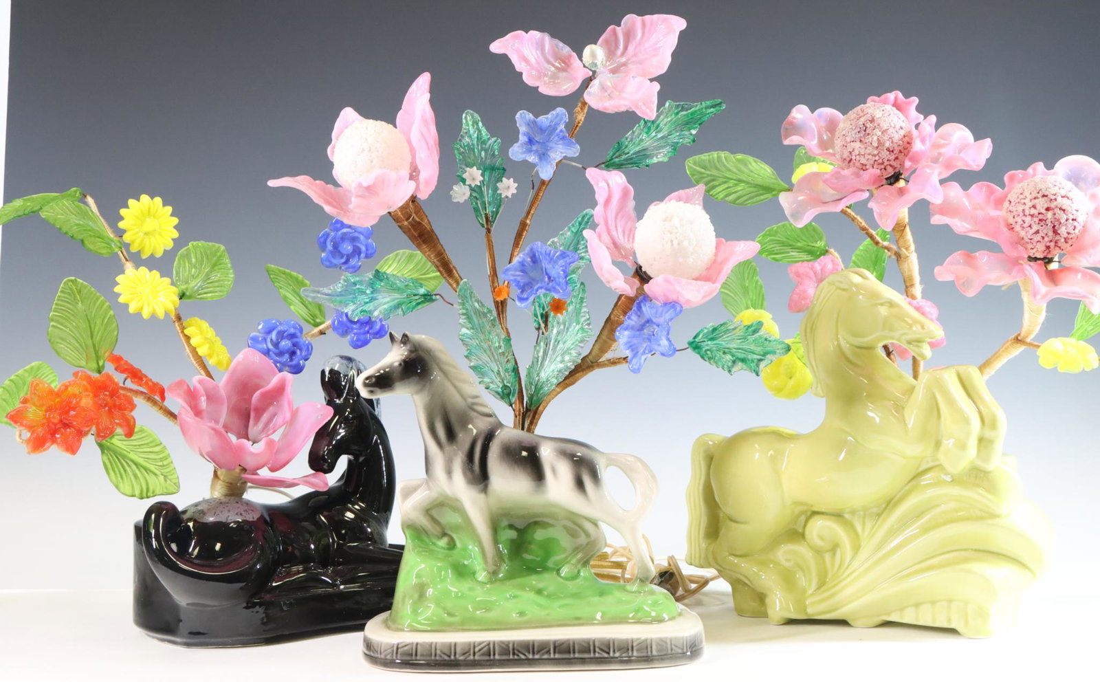 Horse TV Lamps with Glass Flowers: Mid century modern pottery TV lamps (3) of horses in various poses, fitted with art glass flower lamps. The flowers have been set in plaster. All turn on. Sizes range from 12”h to 16”h **P