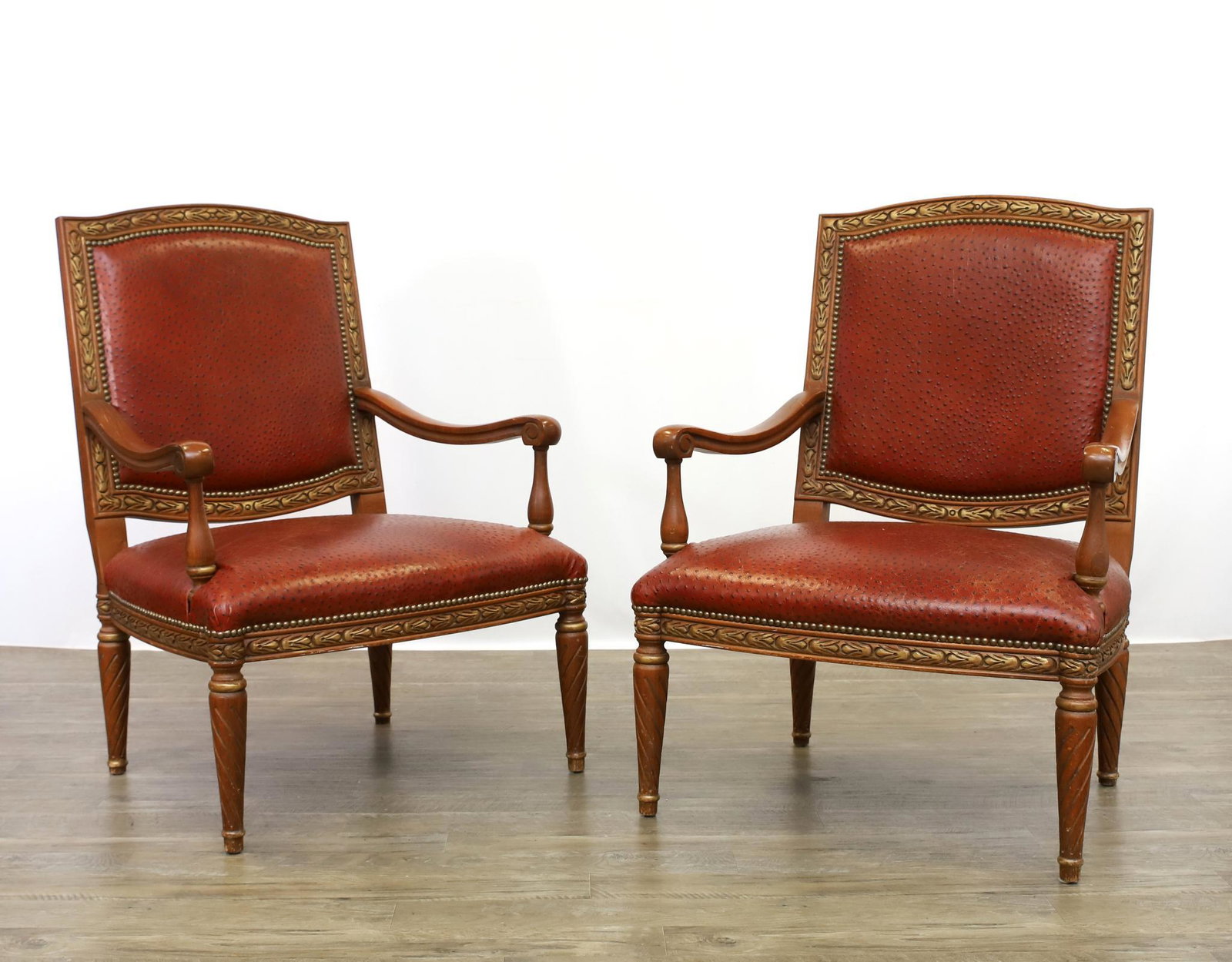 Teak and Ostrich Leather Armchairs: (2) Pair of open armchairs with parcel gilt floral carved frame, scroll arms, tapered round legs, and ostrich leather seat and back with brass tacks. 39.5"h x 28"w x 27"d, seat height 16" **Please Not