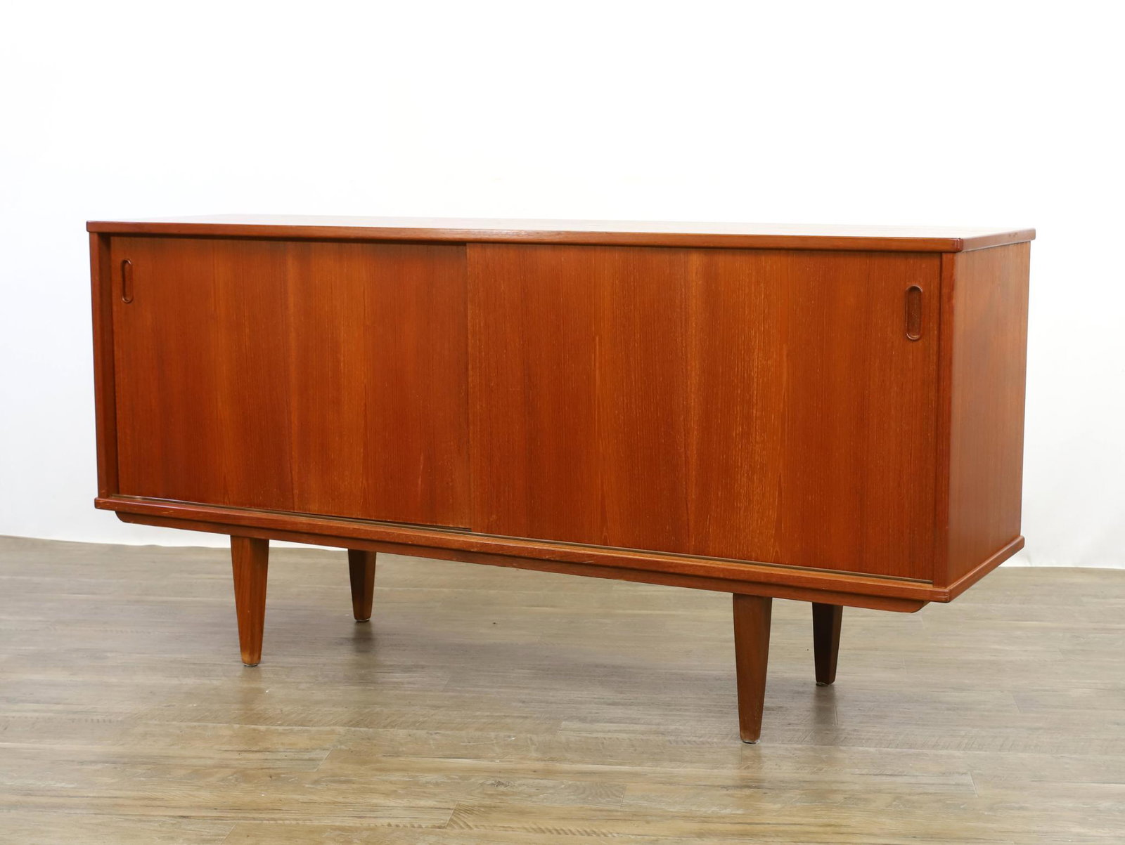 Danish Mid-Century Modern Teakwood Credenza: Two sliding doors with one side having a slide-out drawer and shelving on tapered legs. 30"h x 59.5"w x 16.5"d **Please Note: This item is NOT eligible for in-house shipping. Please refer to the terms
