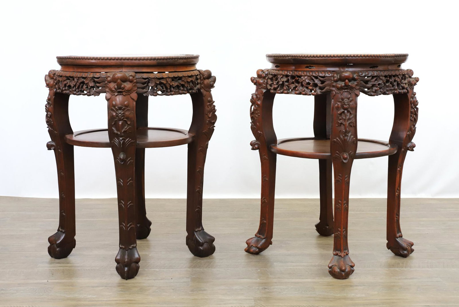 Chinese Carved Rosewood Marble Top Stands: (2) Fraternal pair. Two-tier. Serpentine beaded top with applied foliate decoration insets, foliate and floral carved friezes, dragon motif legs continuing to claw and ball feet. 32"h x 24"round **Ple