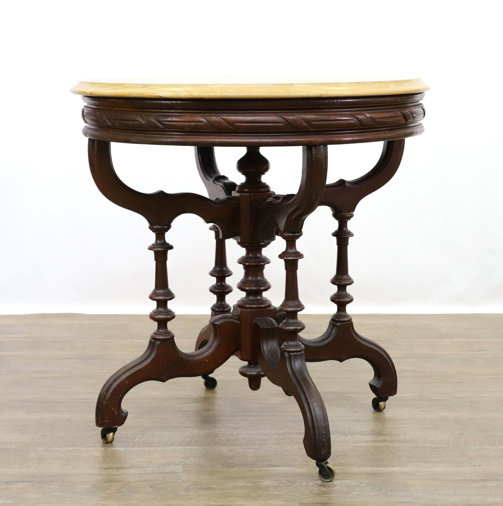 Mahogany Center Table Attributed to Thomas Brooks: Circular beige chamfered marble top, turned pedestal, shaped turned pillars continuing to scrolled legs on brass casters. Hairline cracks to the marble. 30"h x 30"round. **Please Note: This item is NO