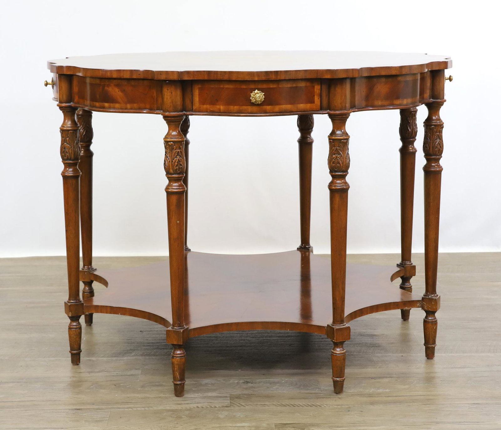 Maitland Smith Figured Mahogany Center Table: Two-tier table having a serpentine top with fan inlay, four drawers, convex second tier with carved tapered block and turned legs. 30.5"h x 42"round **Please Note: This item is NOT eligible for in-hou