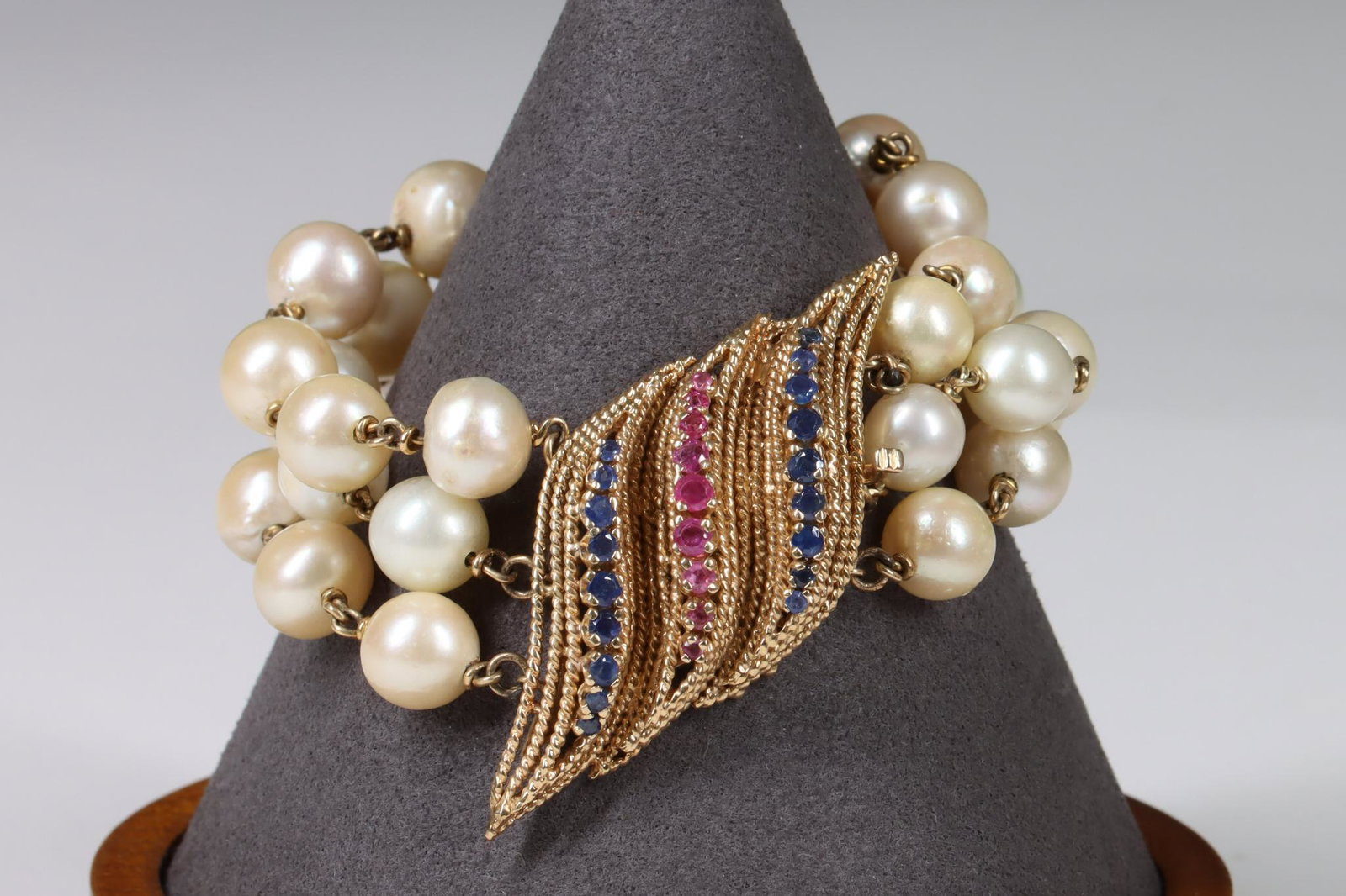 14KY Gold, Pearl, Sapphire and Ruby Bracelet: Bracelet in 14ky gold features 3 strands of chain linked pearls, with a rope design pressure tongue clasp of waves lined with round graduated rubies flanked by blue sapphires. Approx. 7mm - 11mm round