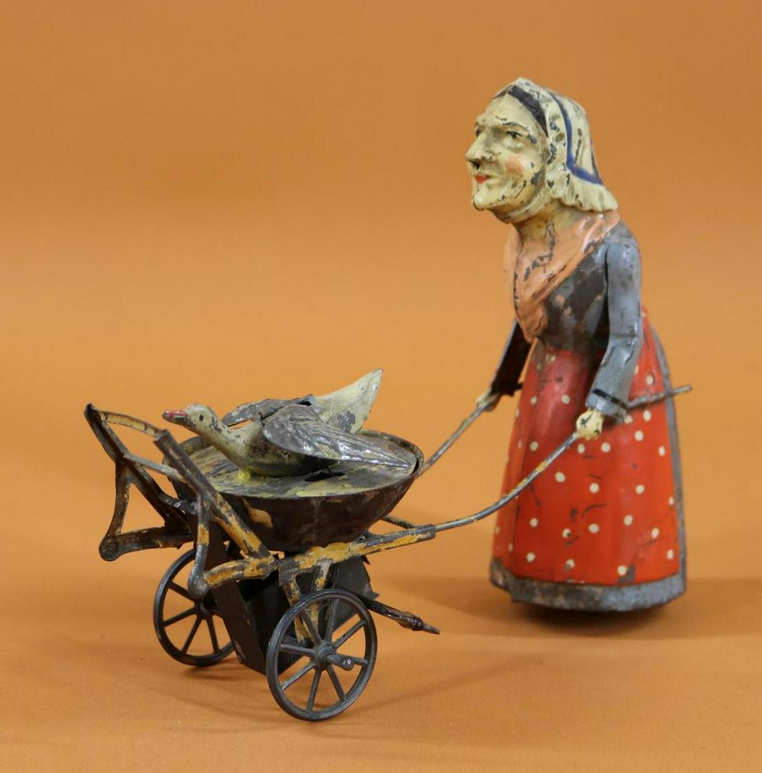 TOY(S).: 6" T x 7" L GUNTHERMANN LADY PUSHING GOOSE IN CART. Painted tin with clockwork mechanism, the goose flaps its' wings as the Lady pushes the cart along. Condition: in good working order. Paint loss. La